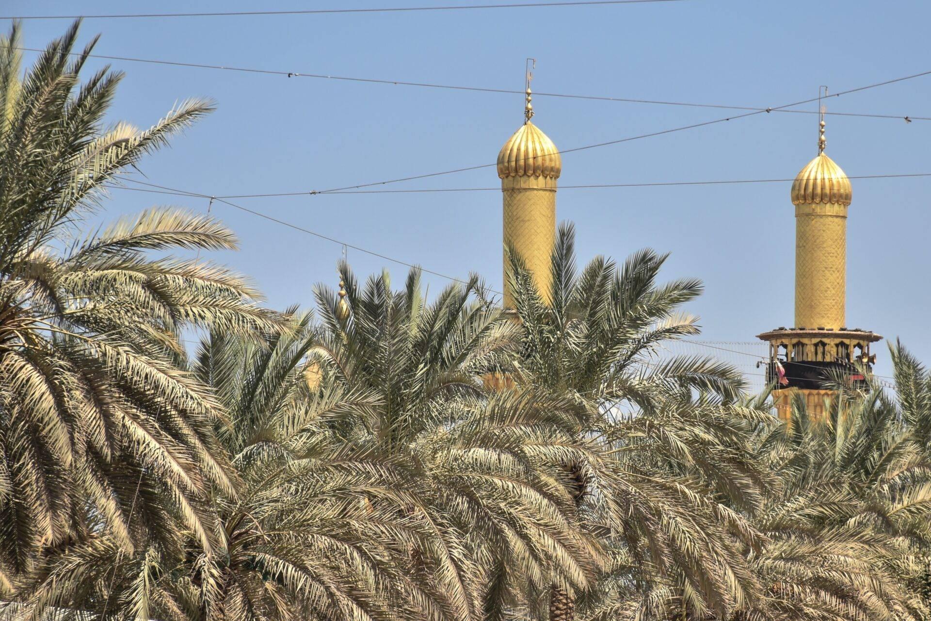 Zwei goldene Minarette mit Zwiebelkuppeln ragen zwischen Dattelpalmen unter blauem Himmel empor