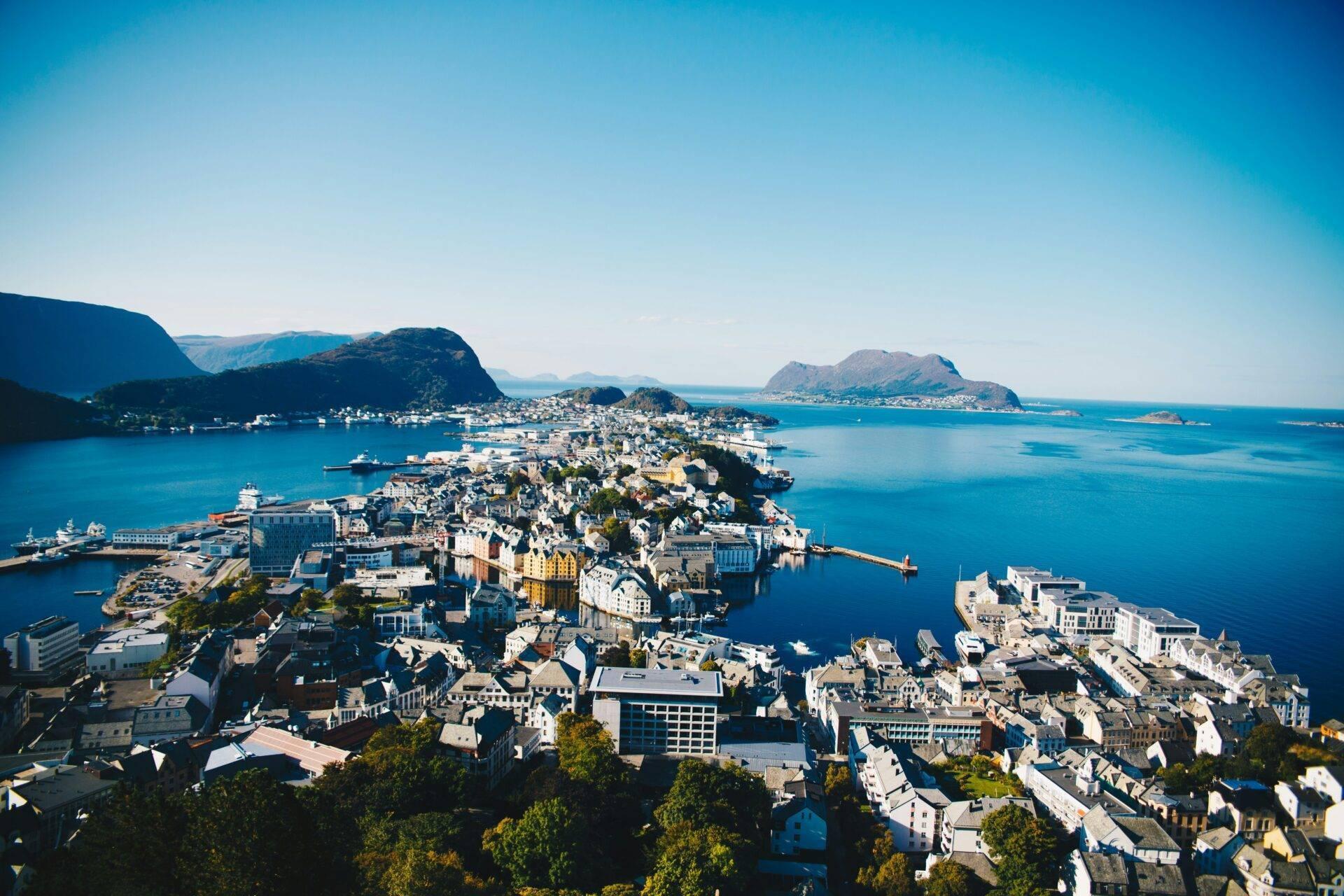 Luftaufnahme einer dicht bebauten norwegischen Küstenstadt auf einer Felshalbinsel, umgeben von blauen Fjorden