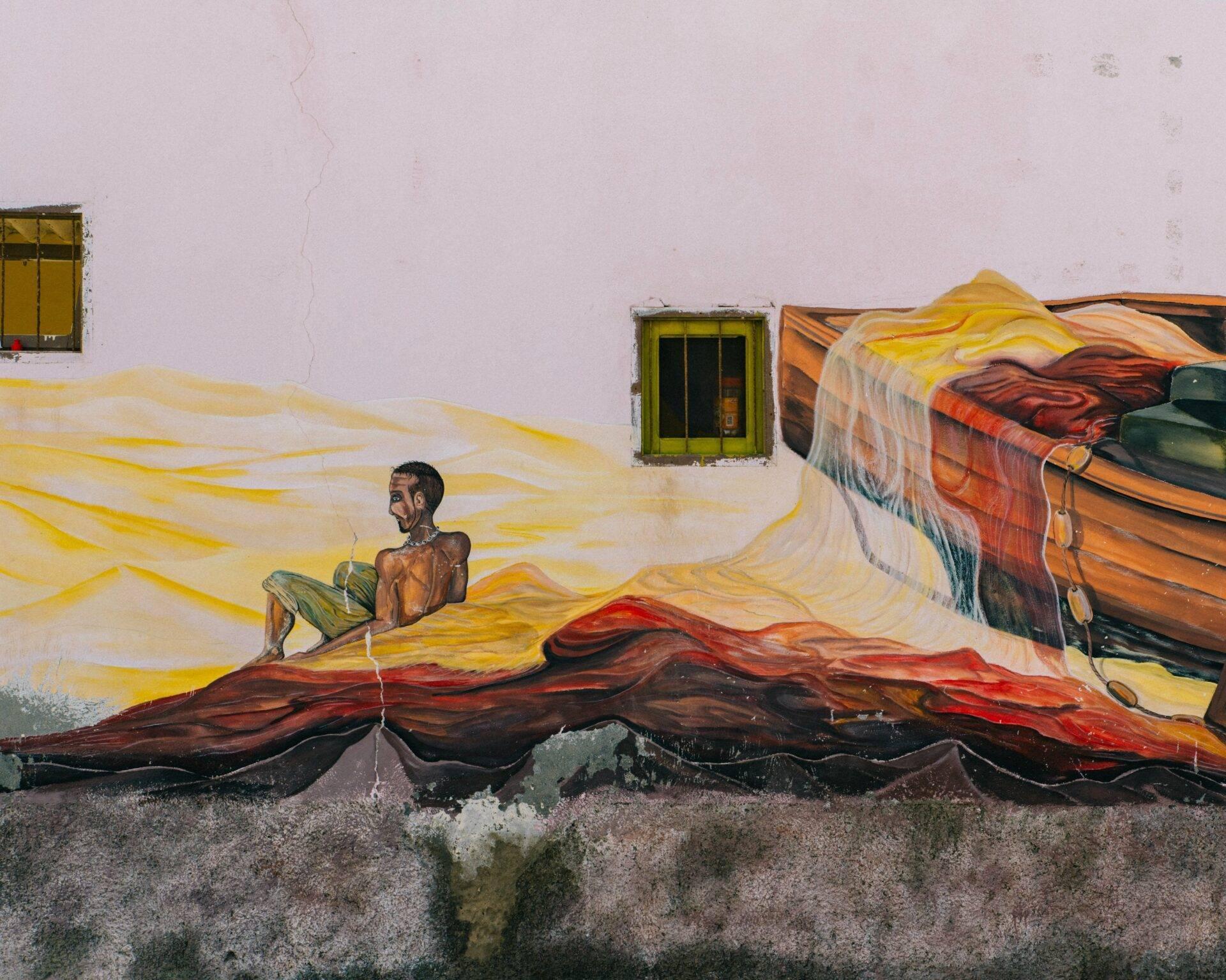 Colourful mural depicting a fisherman and traditional boats on a white coastal facade