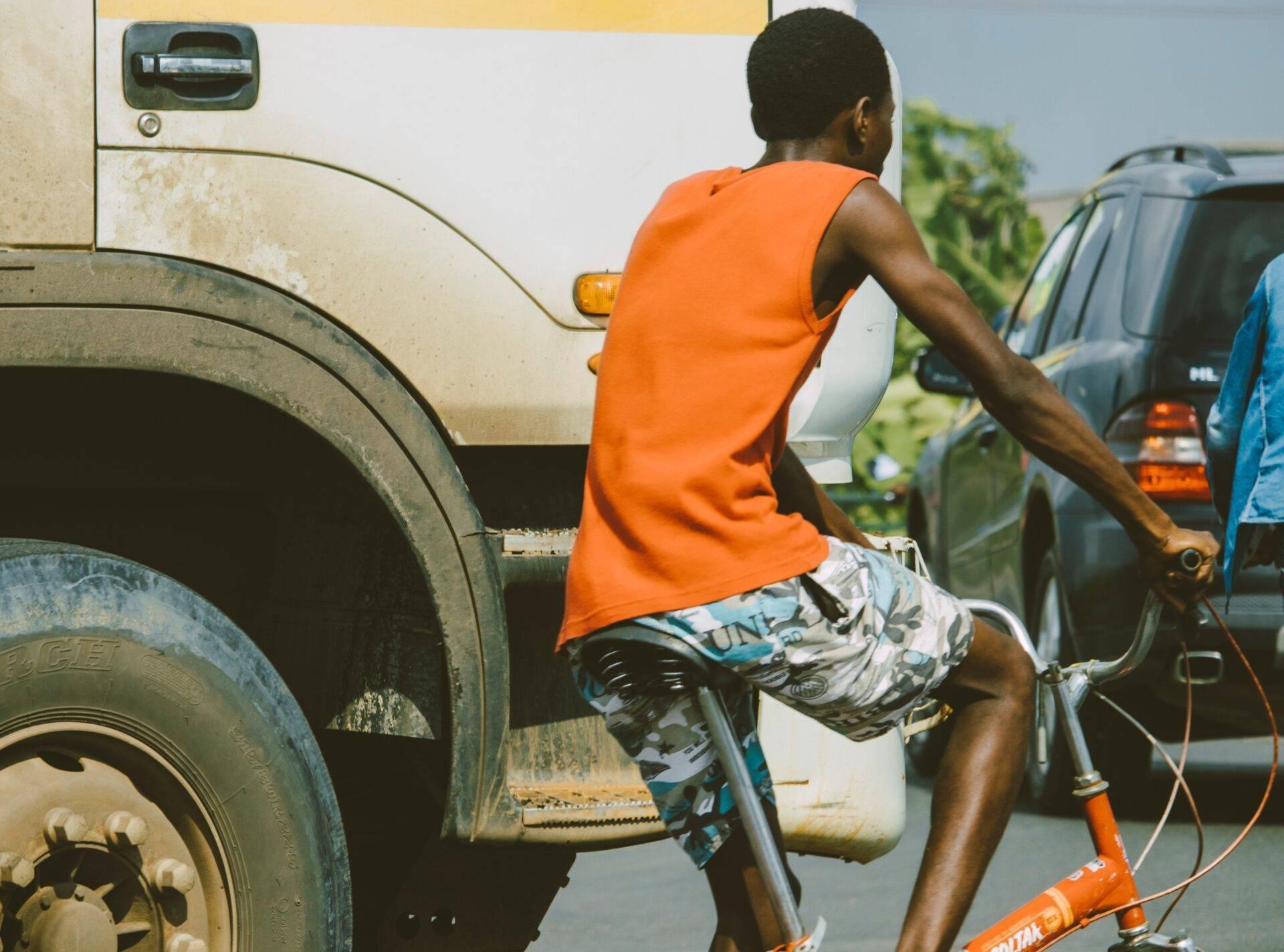 Un joven en bicicleta frente a un camión en una calle animada del África Occidental