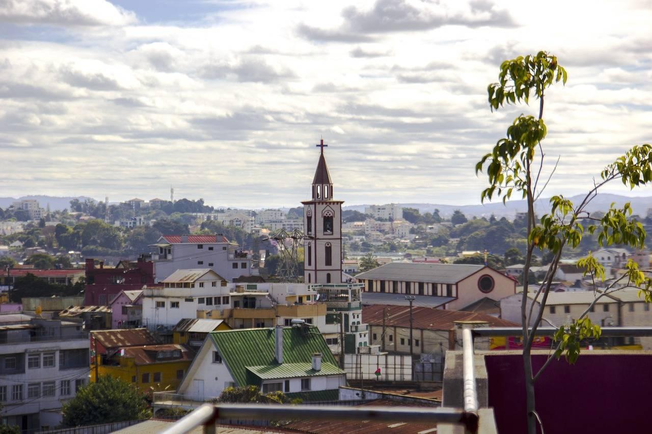 Vista panoramica di una città con una chiesa dal campanile bianco che domina i tetti colorati e il paesaggio montagnoso