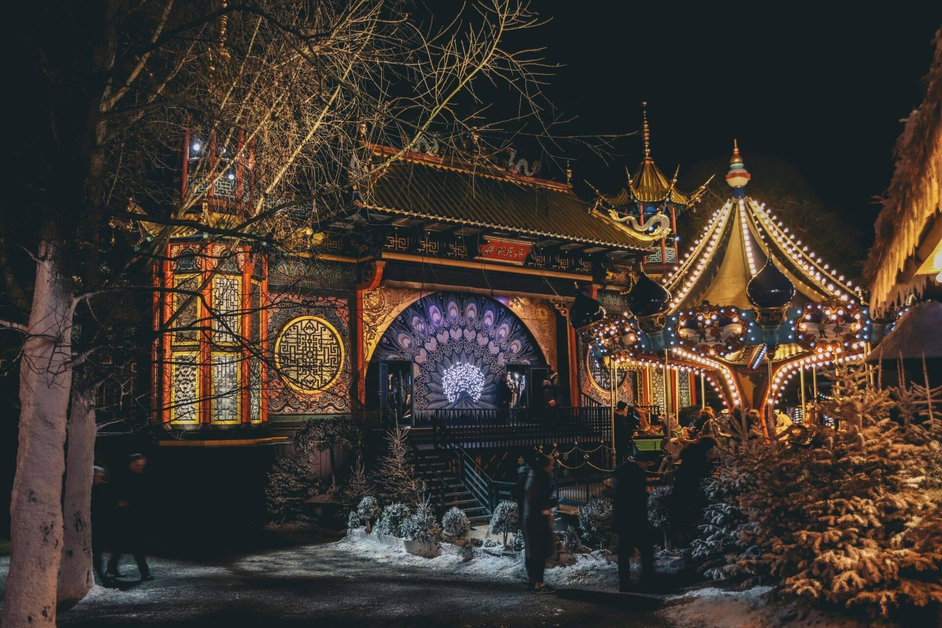 Vista notturna di un parco di divertimenti a tema asiatico illuminato con pagode dorate e decorazioni luminose festive