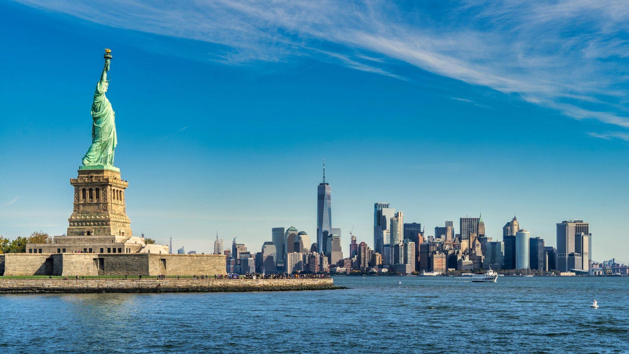 The Statue of Liberty on its island with the Manhattan skyline behind it under a clear blue sky
