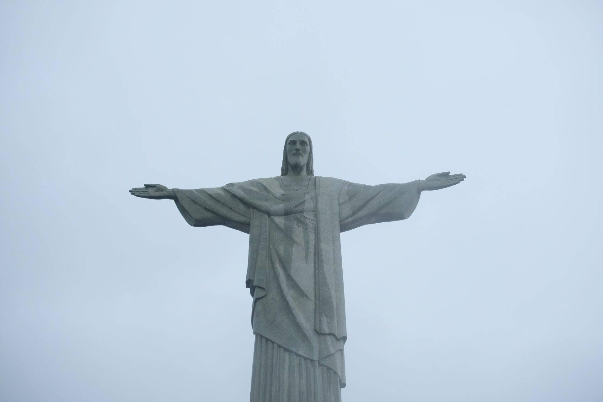Kolossale Statue mit ausgebreiteten Armen, die eine Landschaft unter freiem Himmel überragt, emblematisches brasilianisches Wahrzeichen