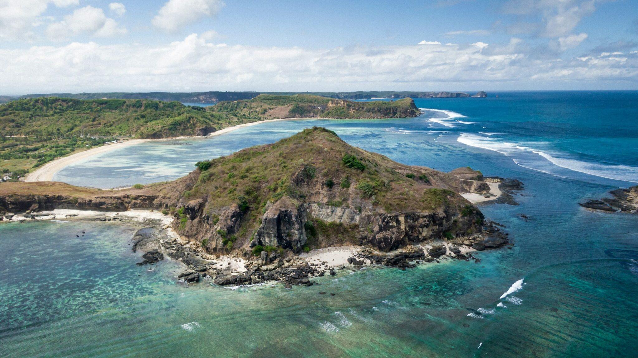 Vista aérea de una isla rocosa y verdoyante rodeada de playas de arena blanca y aguas turquesas bajo un cielo despejado