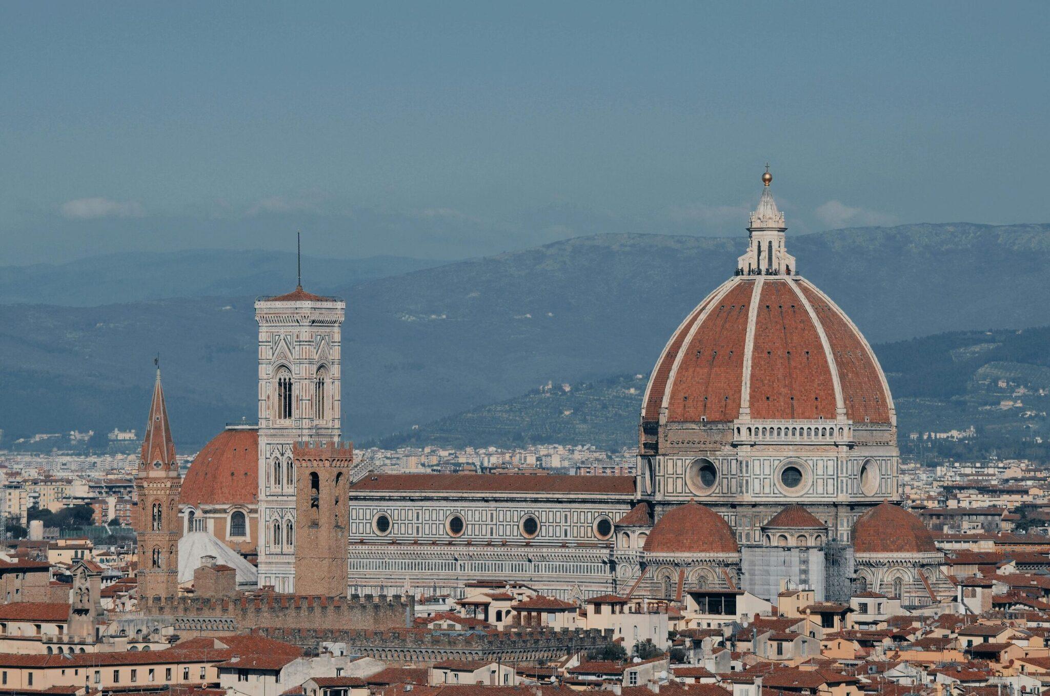Vista panorámica de la catedral con cúpula de terracota y campanile blanco ornamentado dominando la ciudad toscana