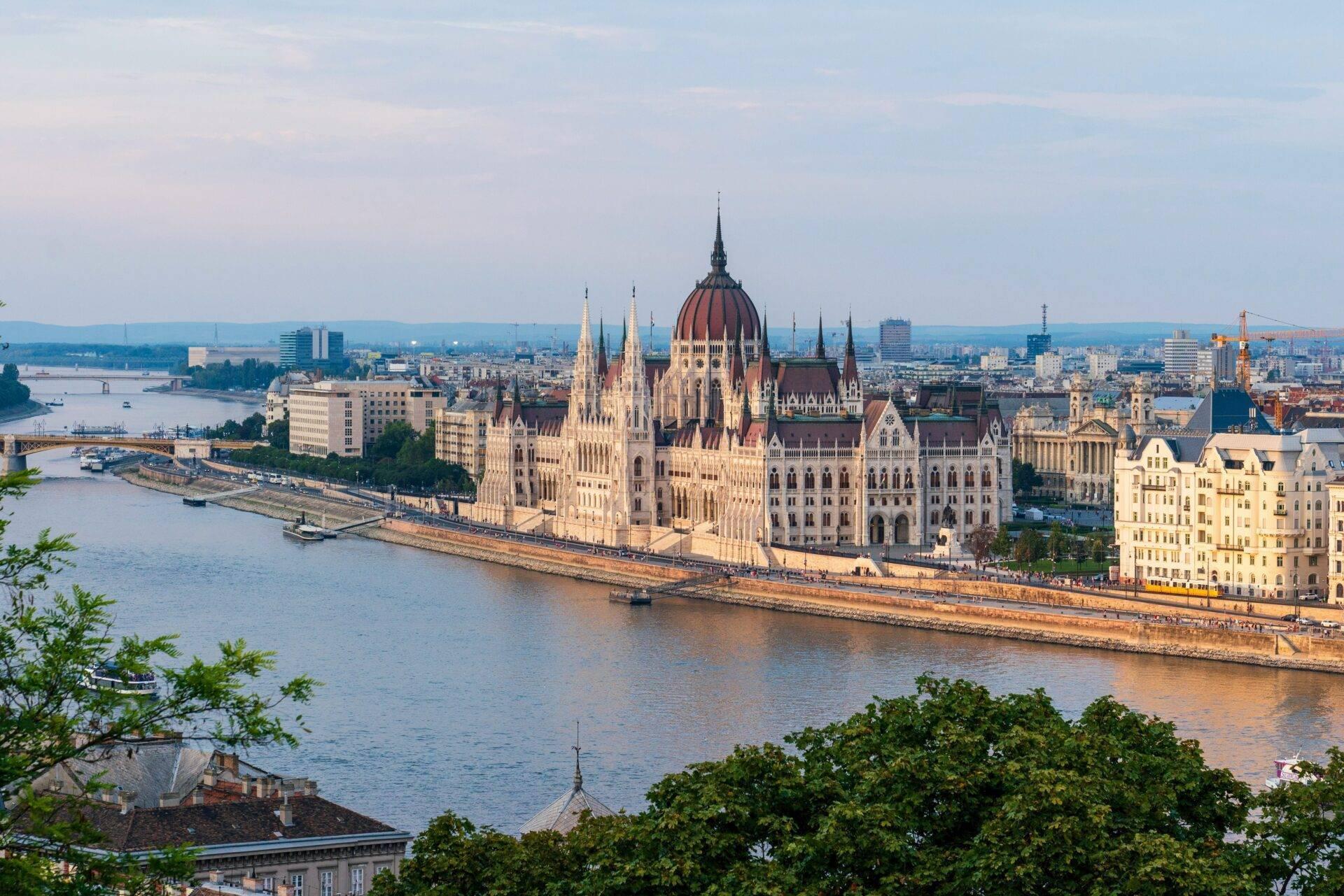Panoramablick auf ein imposantes gotisches Schloss mit spitzen Türmen über einem Fluss mit der Stadt im Hintergrund