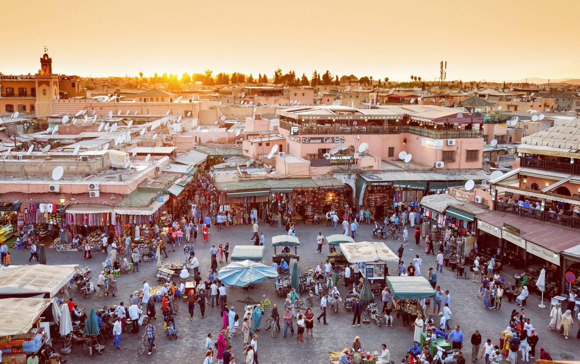 Luftaufnahme einer belebten marokkanischen Medina mit Markt, ockerfarbenen Gebäuden und Besuchermenge bei Sonnenuntergang