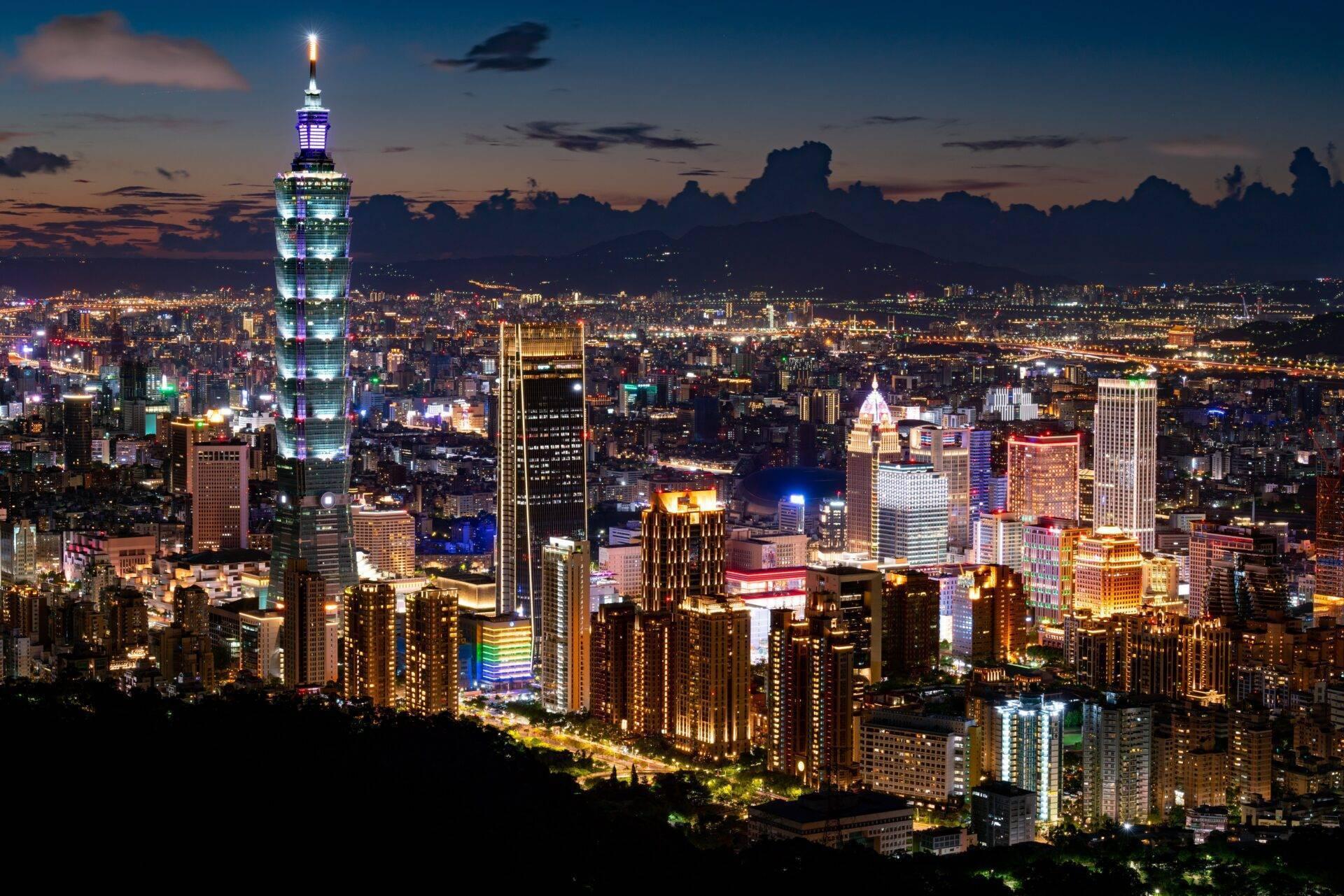 Vista notturna di una metropoli asiatica illuminata con una torre distintiva accesa in blu che domina lo skyline urbano