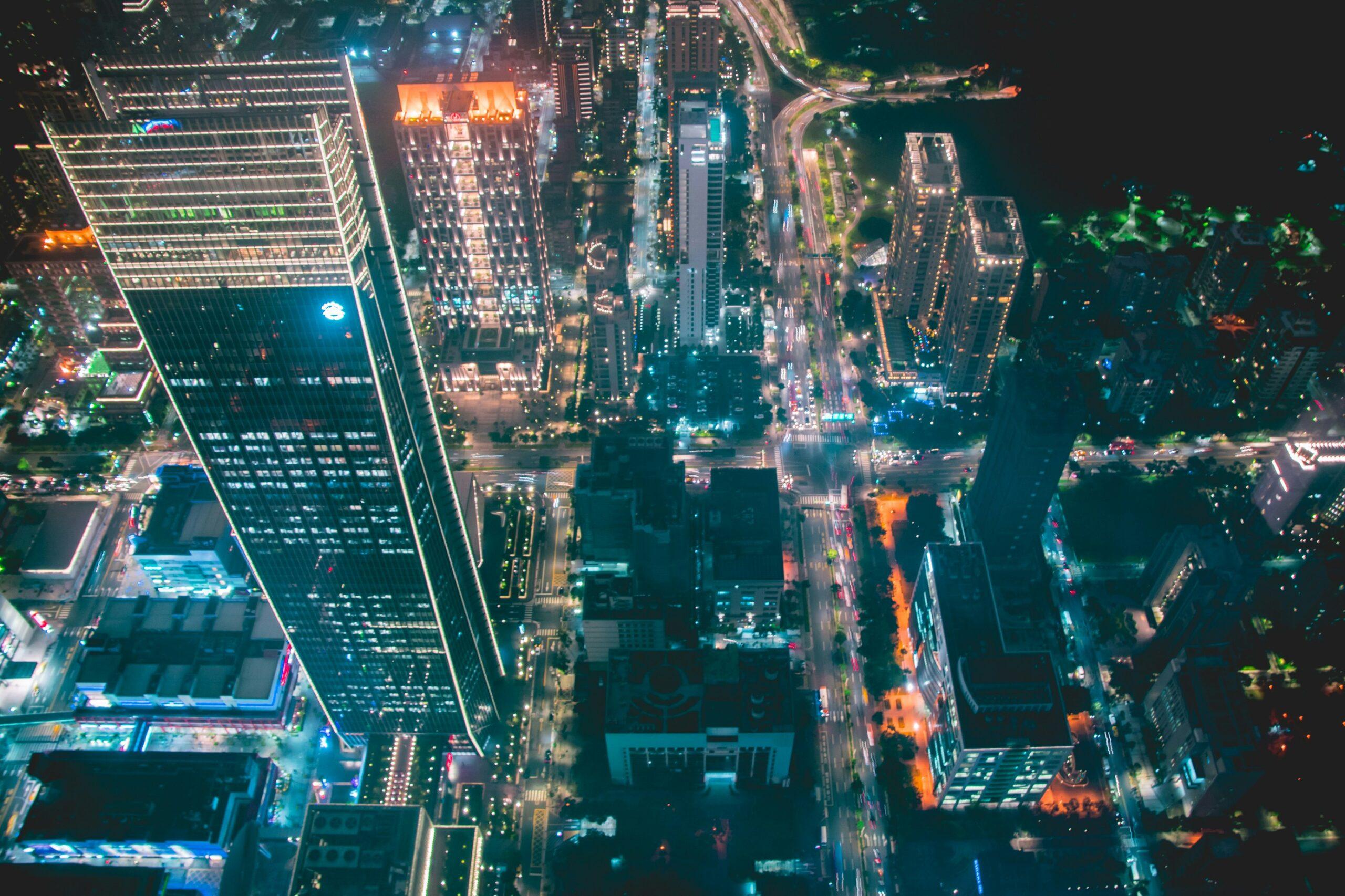 Vista aérea nocturna de una metrópolis asiática con rascacielos iluminados, calles animadas y paseo fluvial