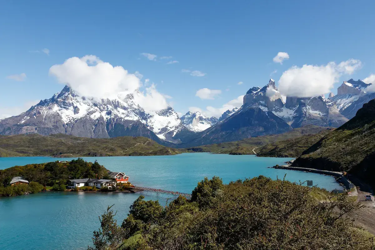 Lago turquesa rodeado de montañas nevadas con lodge y vegetación verde bajo cielo despejado