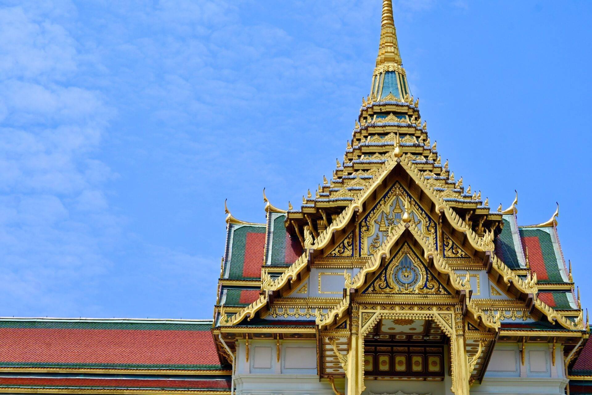 Un tempio buddista thailandese con tetti dorati ornati, tegole colorate e architettura tradizionale sotto un cielo azzurro