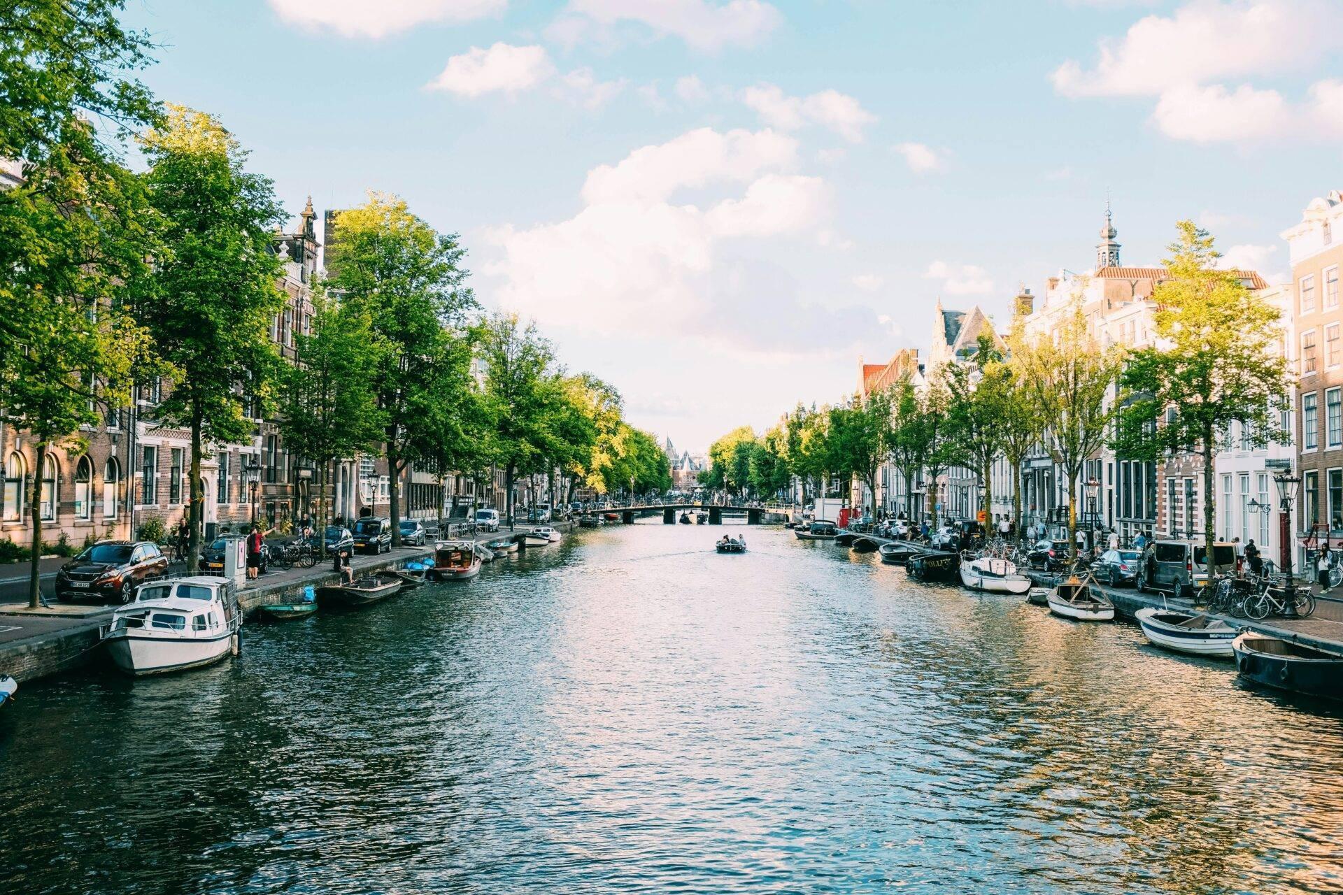 Städtische Gracht mit bunten Häusern, festgemachten Booten und grünen Bäumen unter blauem Himmel