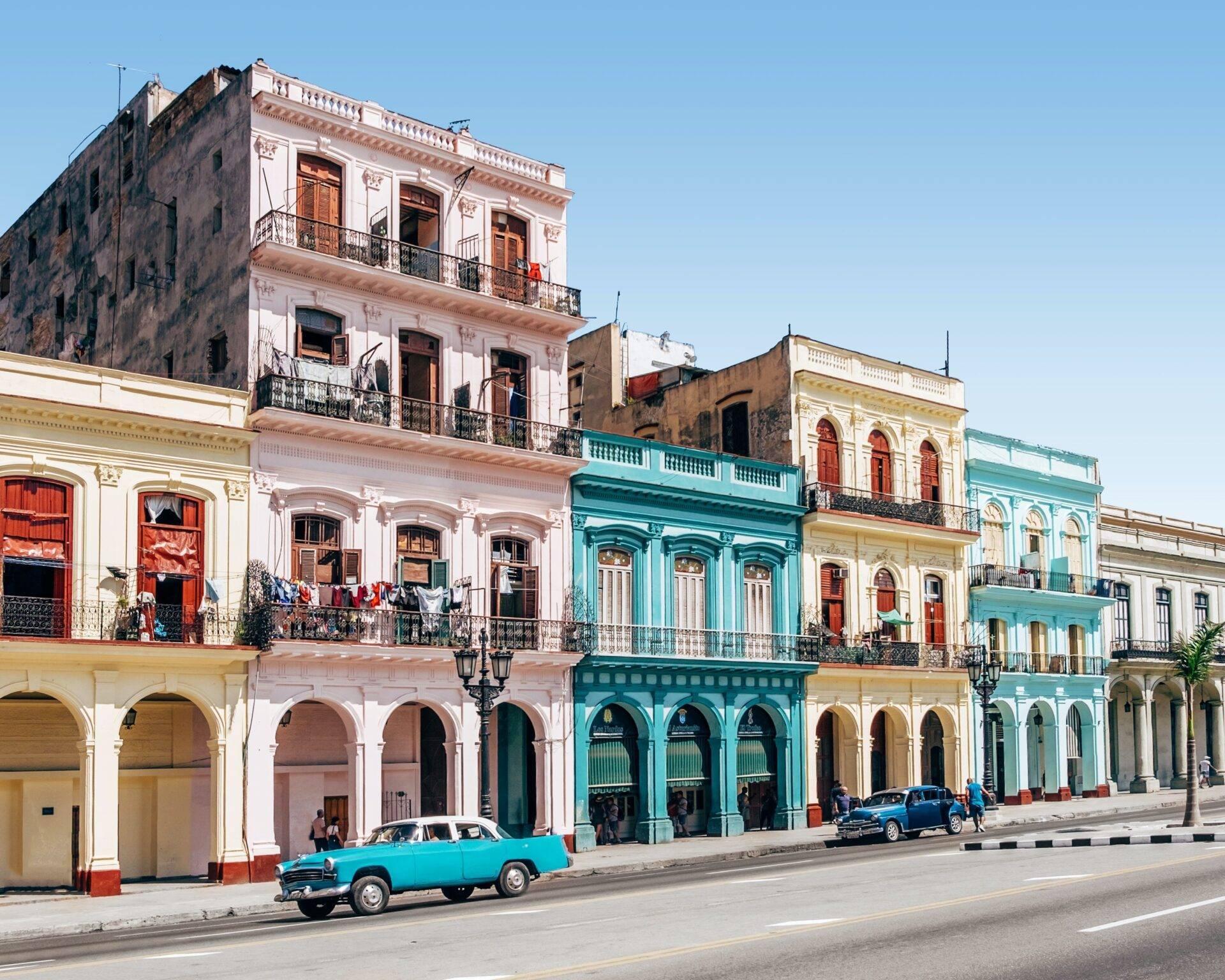 Una strada coloniale con edifici dai colori pastello e un’auto d’epoca color turchese