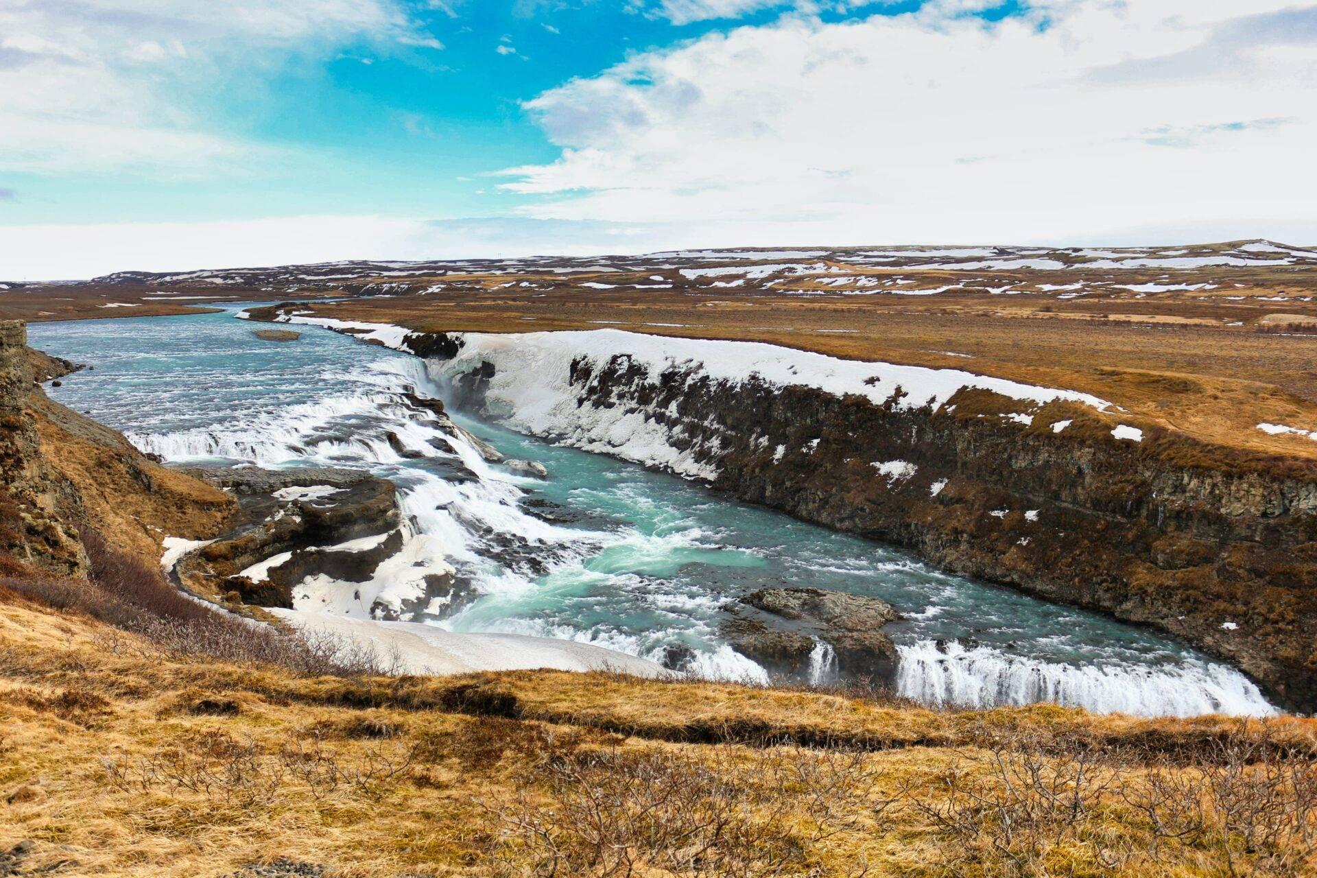 Un río turquesa glaciar serpentea entre acantilados nevados en un paisaje islandés de tundra desértica