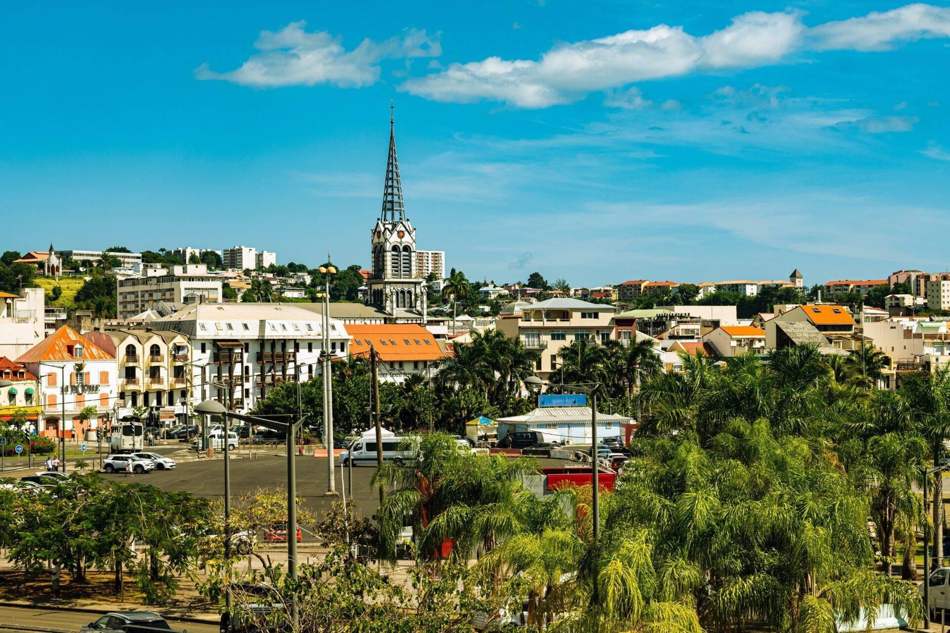 Panoramablick auf eine Küstenstadt mit orangefarbenen Kirchendächern, Palmen, Kolonialarchitektur und klarem blauem Himmel