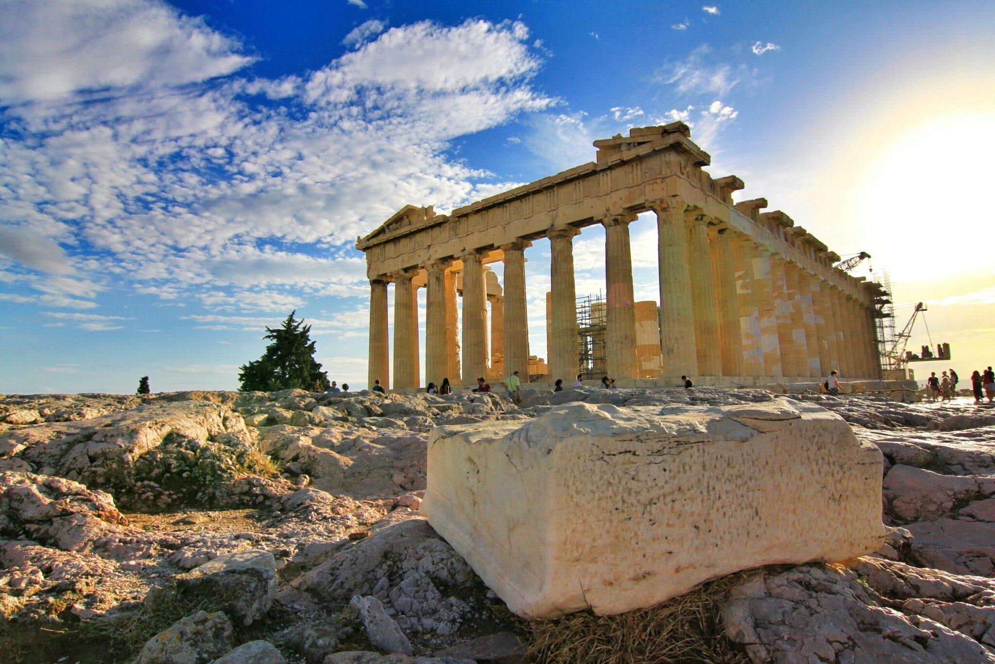 Die antiken Ruinen des Parthenon überragen eine felsige Landschaft unter bewölktem blauem Himmel mit Besuchern