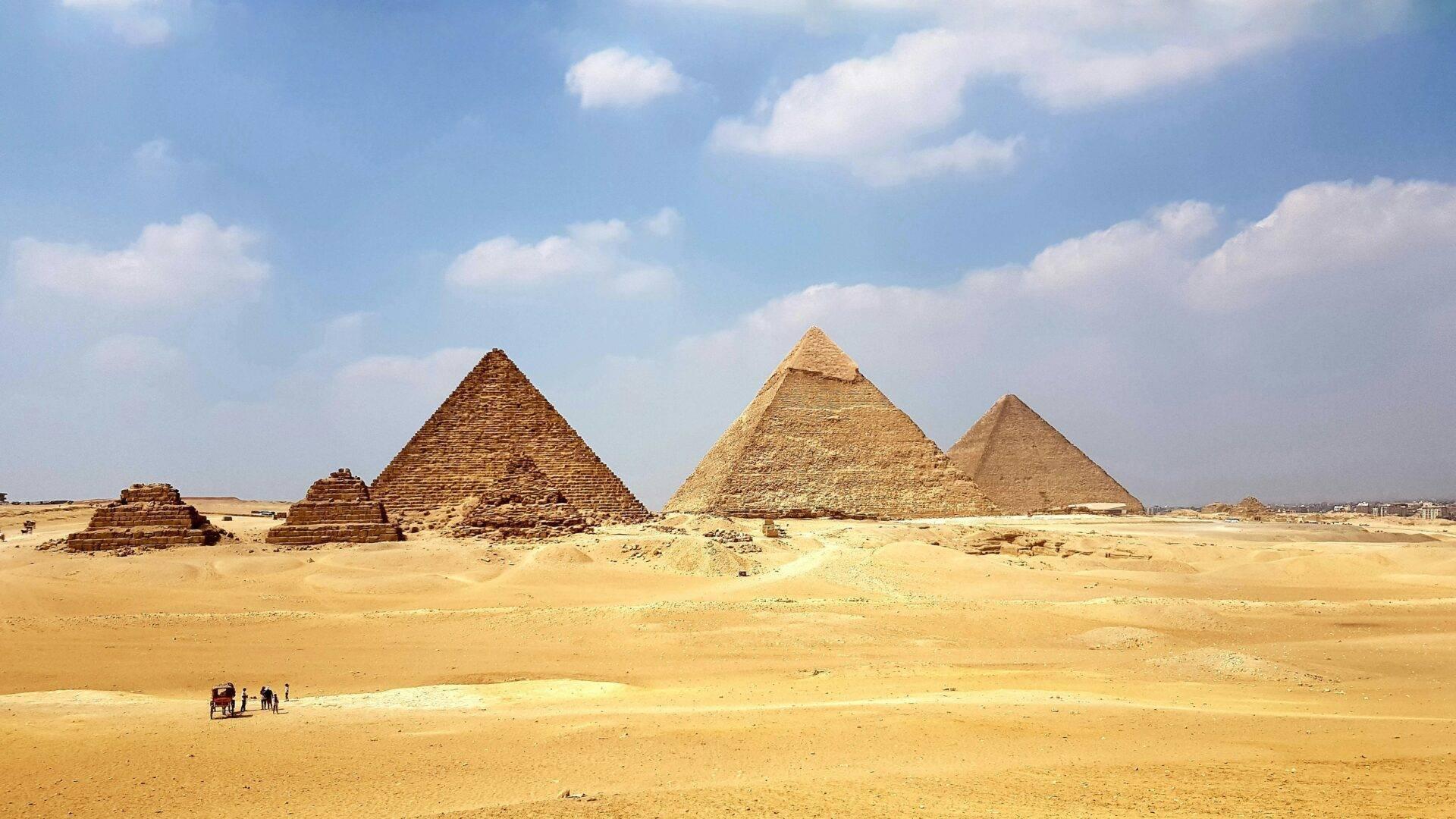 Tre piramidi di pietra in un deserto arido sotto un cielo azzurro con alcuni visitatori