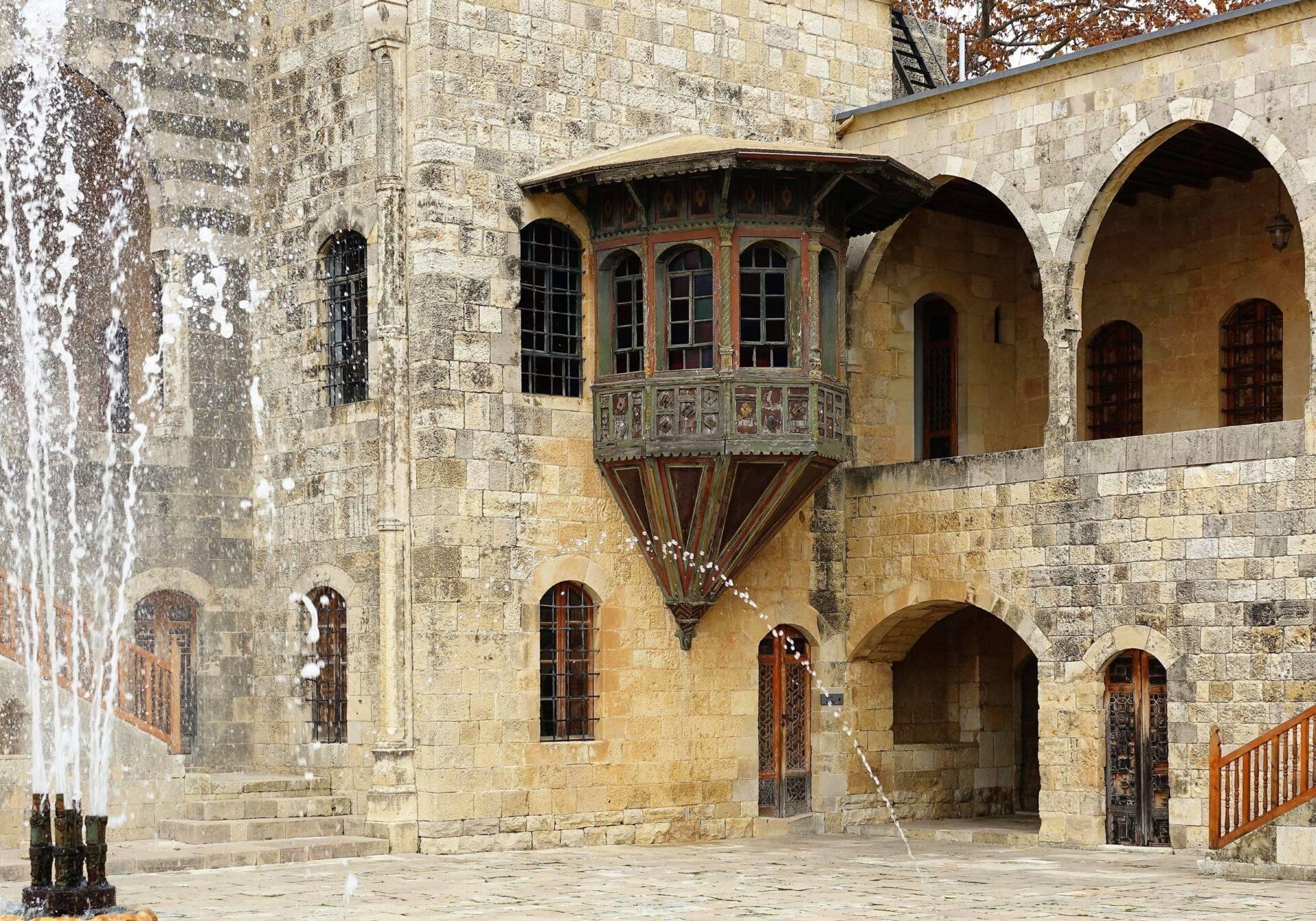 Patio interior de una fortaleza medieval con arquerías de piedra, ventanas ornamentadas y balcón suspendido decorado