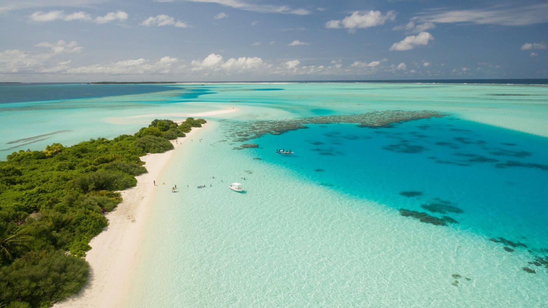 Luftaufnahme einer tropischen Insel mit weißem Sandstrand, kristallklarem türkisfarbenem Lagunen, üppiger Vegetation und einigen sichtbaren Booten