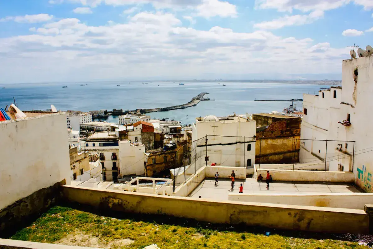 Vista aérea de una ciudad costera mediterránea con puerto, edificios blancos y niños jugando en un patio