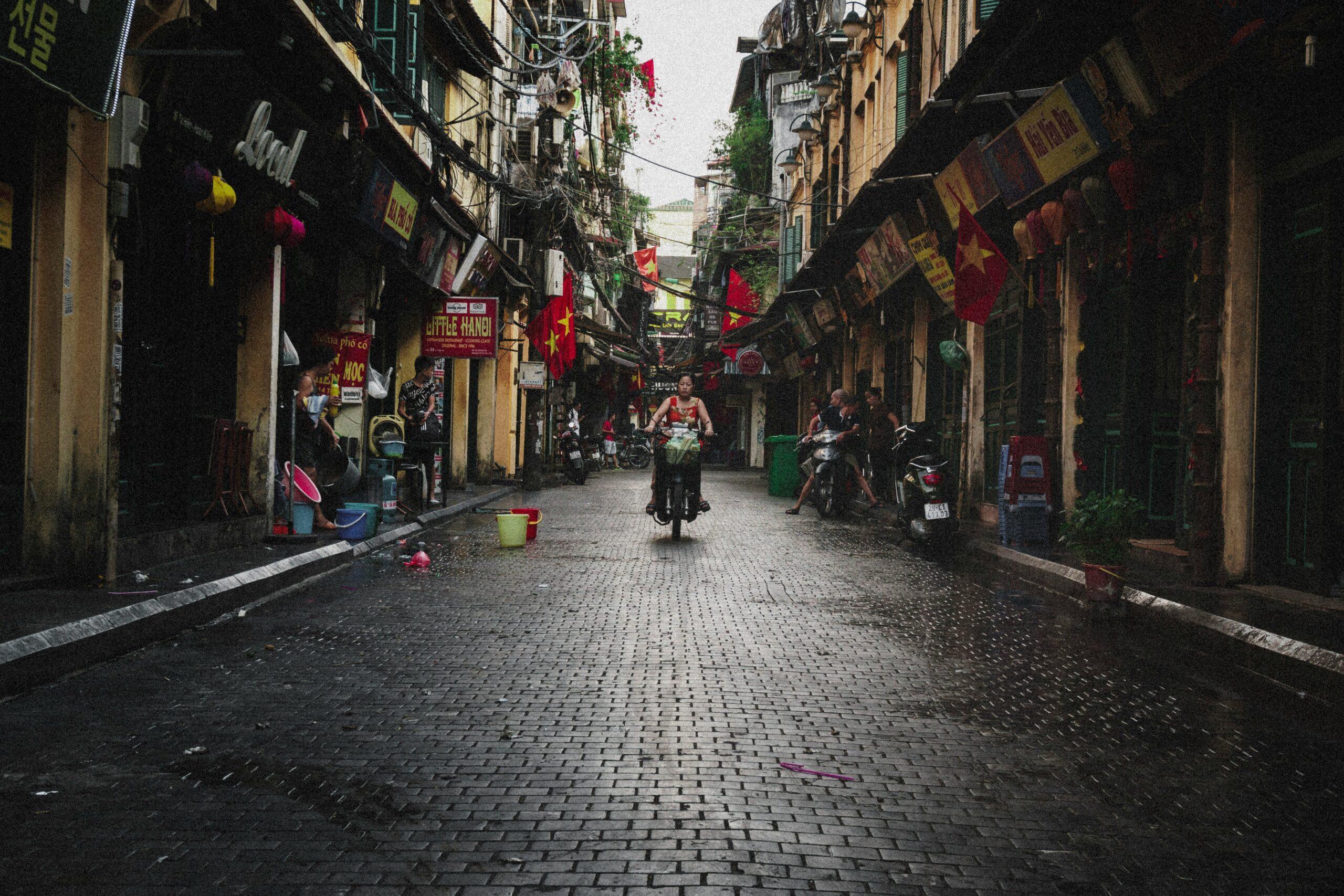 Callejuela estrecha del Barrio Antiguo con fachadas amarillas, banderas rojas y motos, ambiente urbano auténtico de Asia