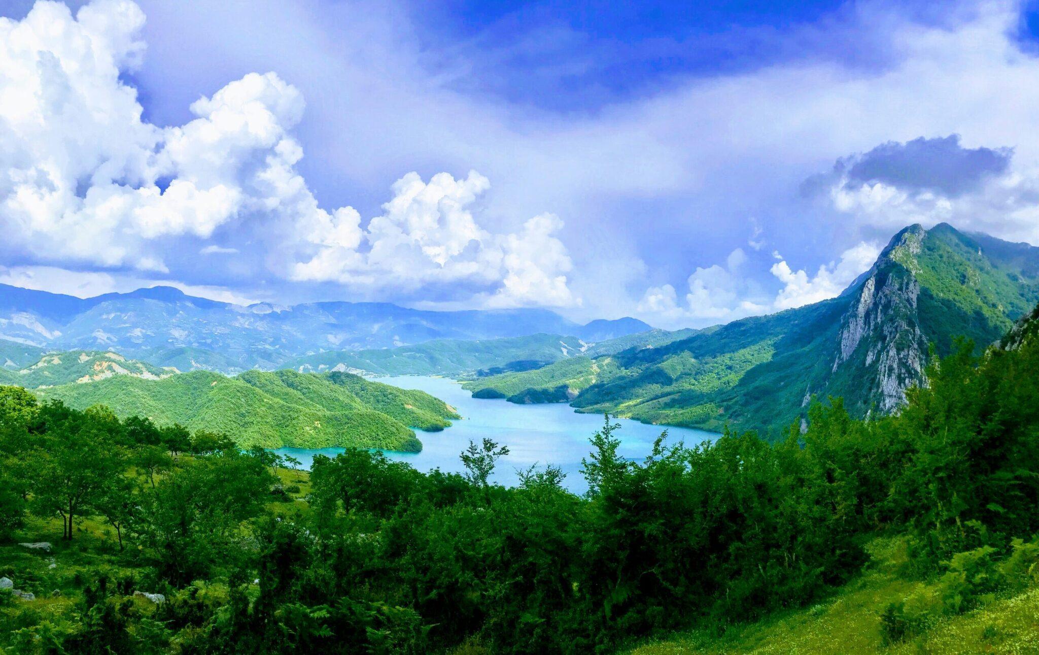 Panoramablick auf einen türkisblauen Alpensee, umgeben von grünen Bergen und einer imposanten Felswand