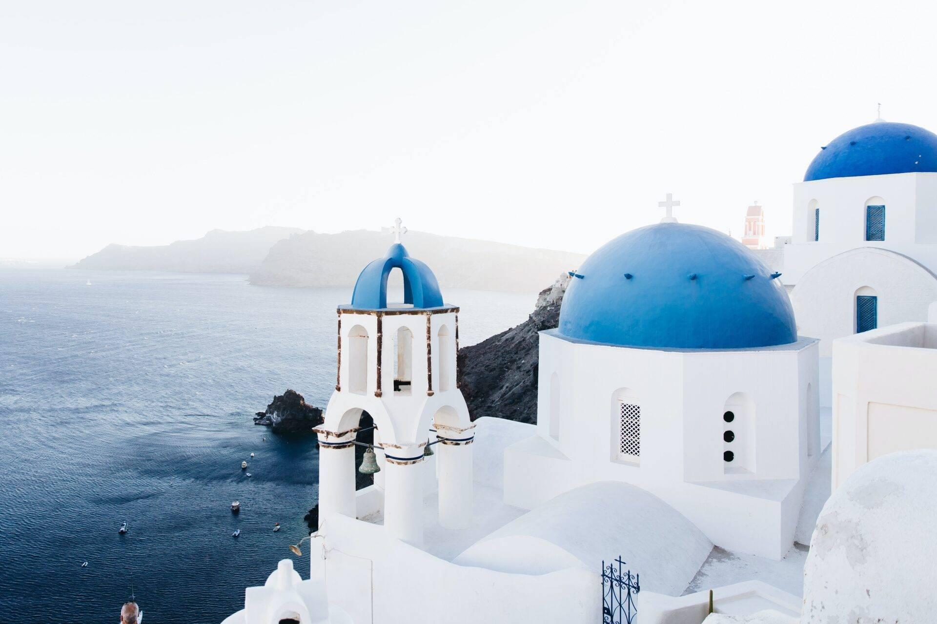 Weiße Kirchen mit blauen Kuppeln über dem Mittelmeer, typisch zykladische Architektur der griechischen Inseln