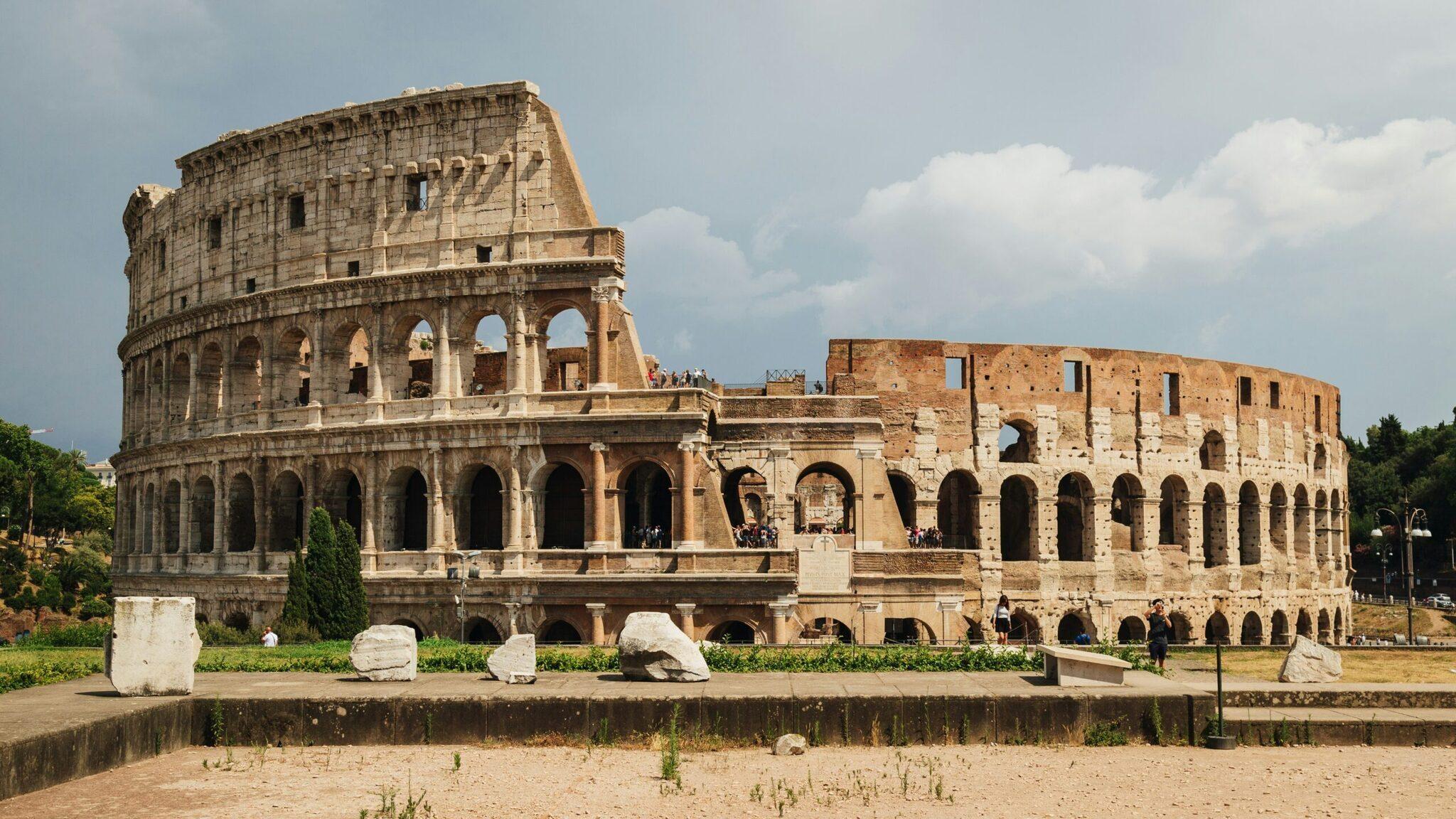 Las majestuosas ruinas del Coliseo romano con sus arcadas y gradas parcialmente conservadas bajo un cielo azul