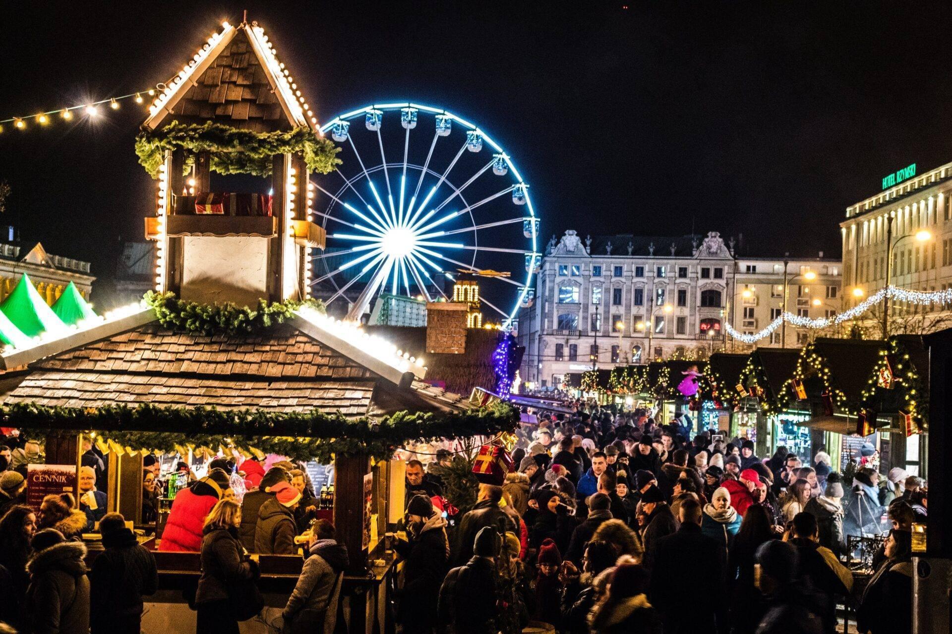 Un mercado navideño iluminado de noche con una gran noria azul, casetas decoradas y ambiente festivo