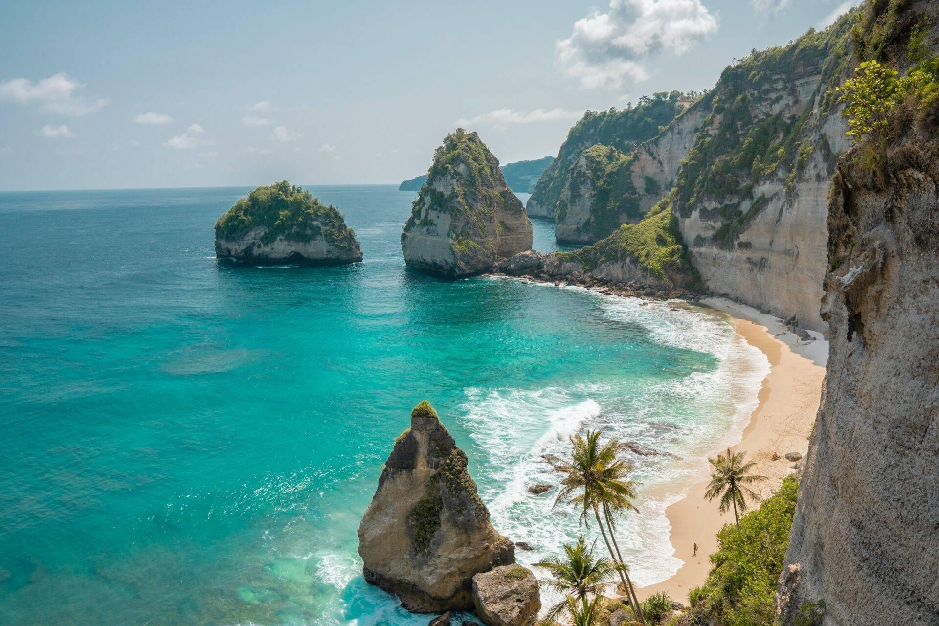 Spiaggia tropicale con falesie calcaree bianche, isolotti rocciosi e acque turchesi cristalline bordate di palme