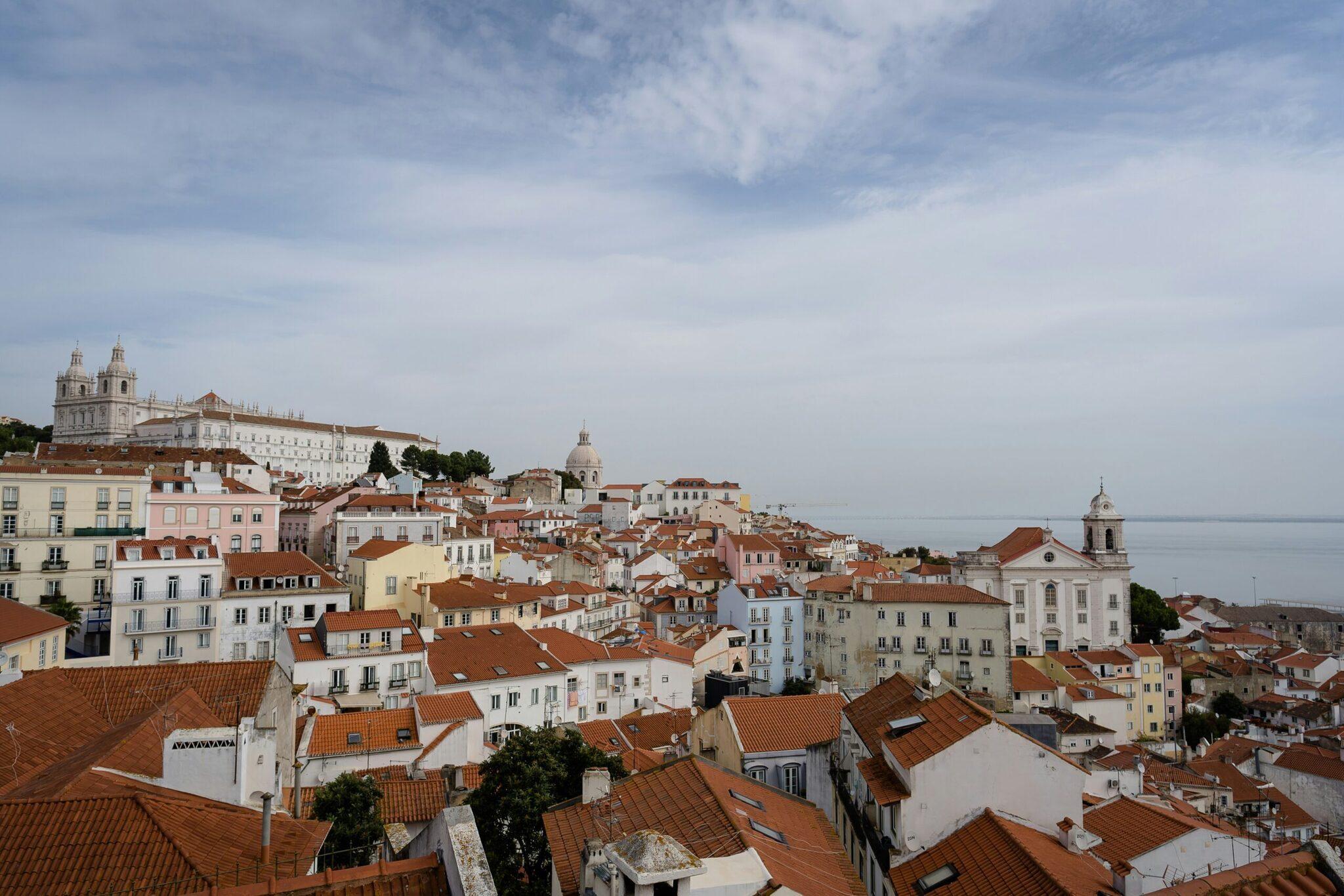 Panoramablick über eine europäische Altstadt mit roten Ziegeldächern und markanten Kirchturmssilhouetten unter bewölktem Himmel