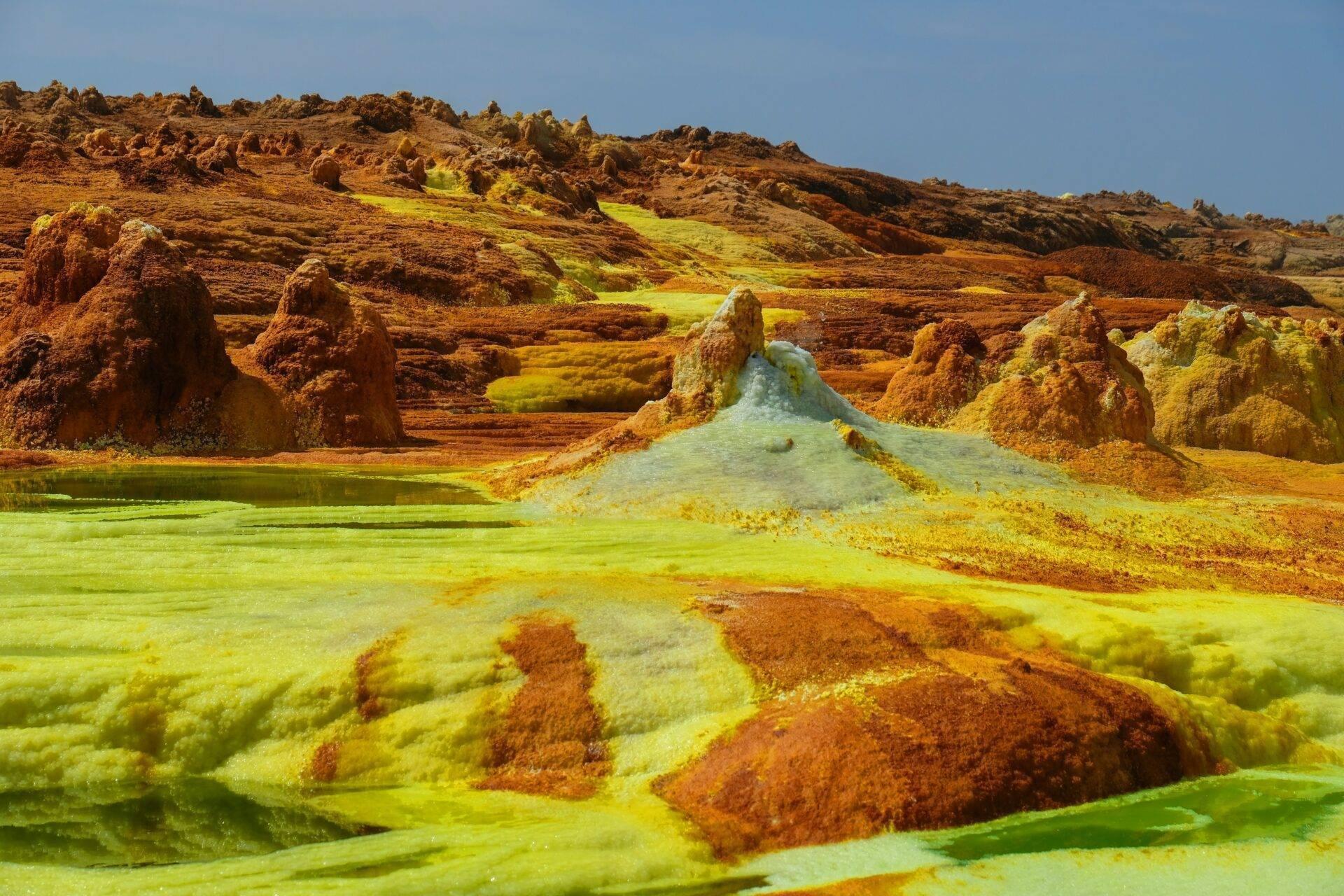 Paisaje geotérmico con fuentes termales teñidas de azufre amarillo y rocas de tonos ocre rojizo