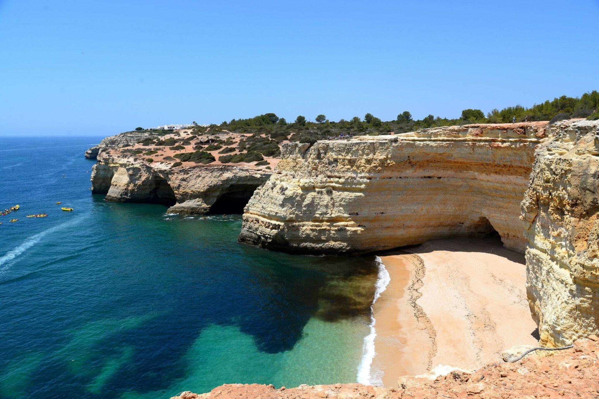 A small golden sandy beach nestled between limestone cliffs and crystal-clear turquoise water under a blue sky