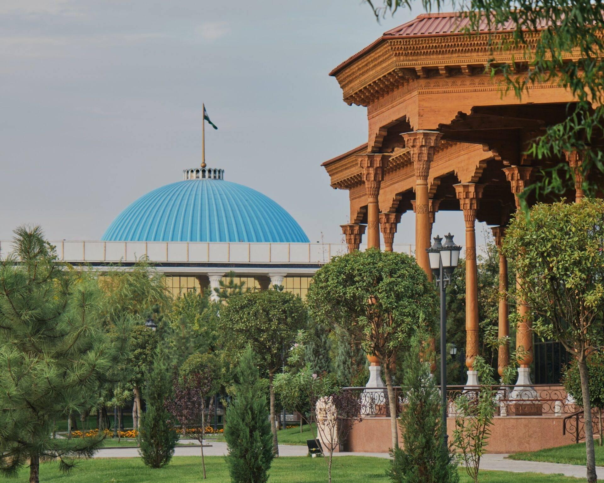 Grüner Park mit Säulenpavillon aus roten Backsteinen und modernem Gebäude mit türkisfarbener Kuppel