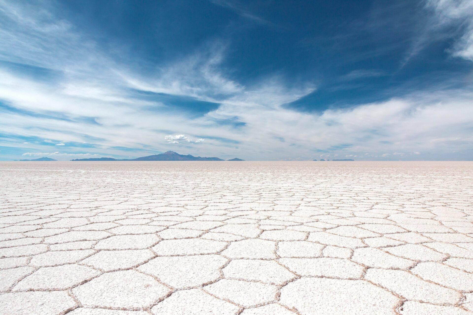 Immensa pianura di sale bianco screpolato con montagne lontane sotto un cielo azzurro con nuvole