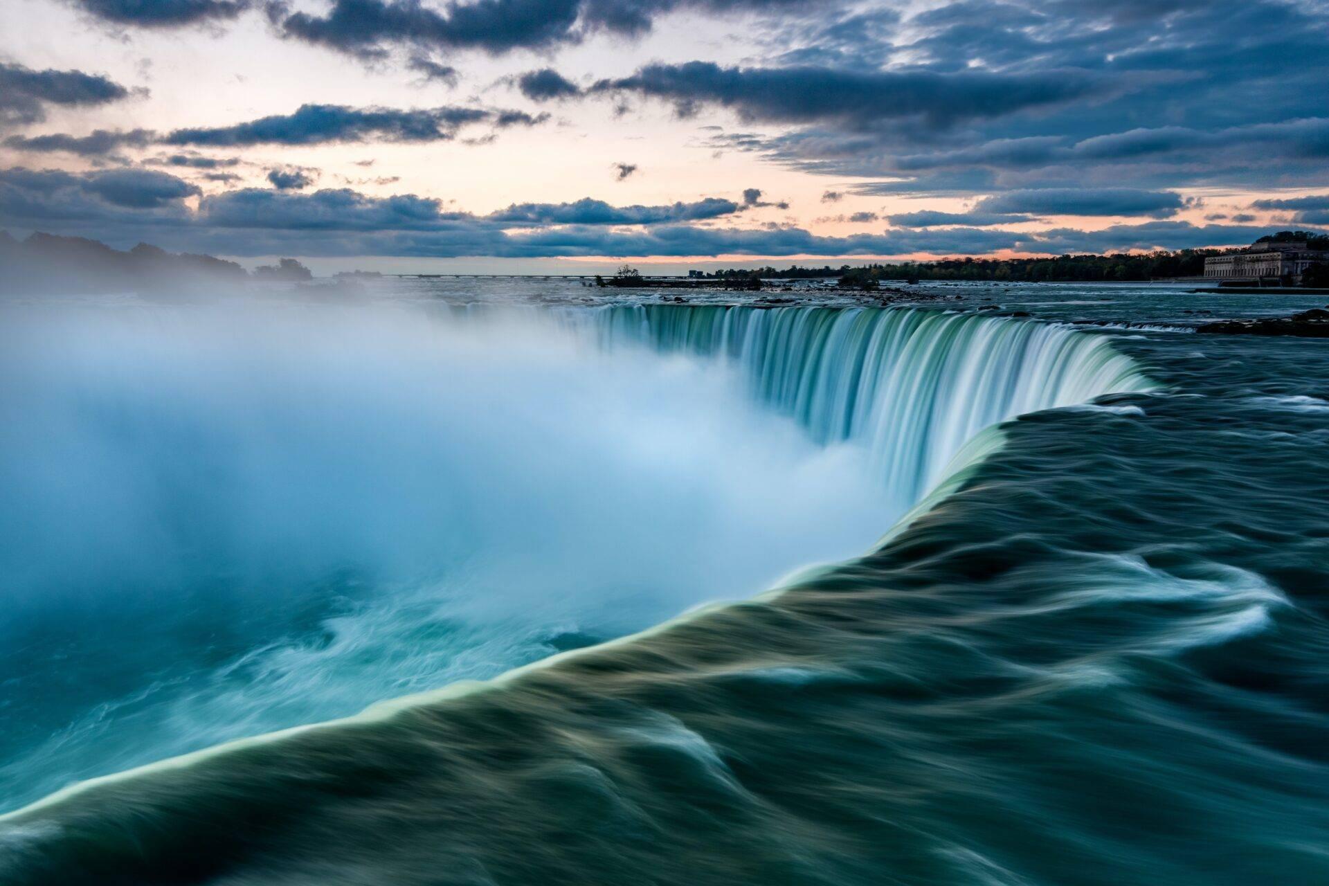 Ein majestätischer türkisfarbener Wasserfall stürzt in eine riesige Kaskade unter einem bewölkten Abendhimmel
