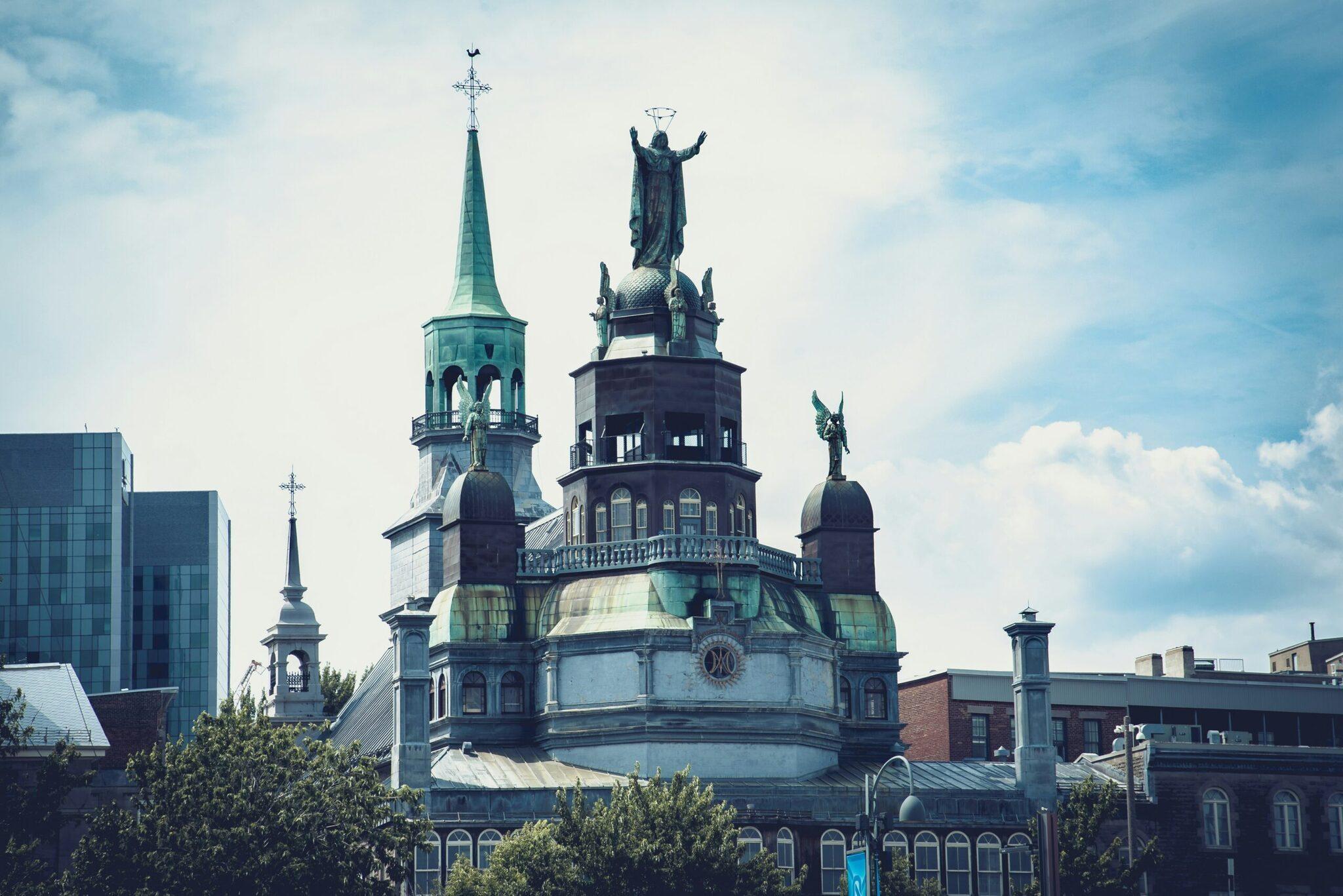 Kathedrale mit türkisgrüner Kupferkuppel und Engelsfigur, die über die Stadtsilhouette ragt, unter bewölktem blauem Himmel