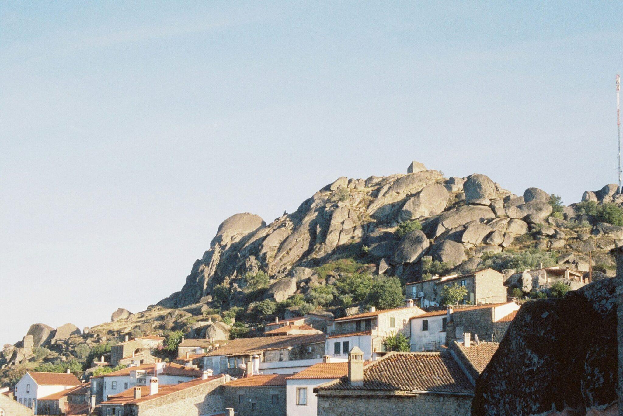 Un pueblo de casas blancas con tejados rojos construidas en la ladera de una montaña rocosa salpicada de enormes bolos de granito