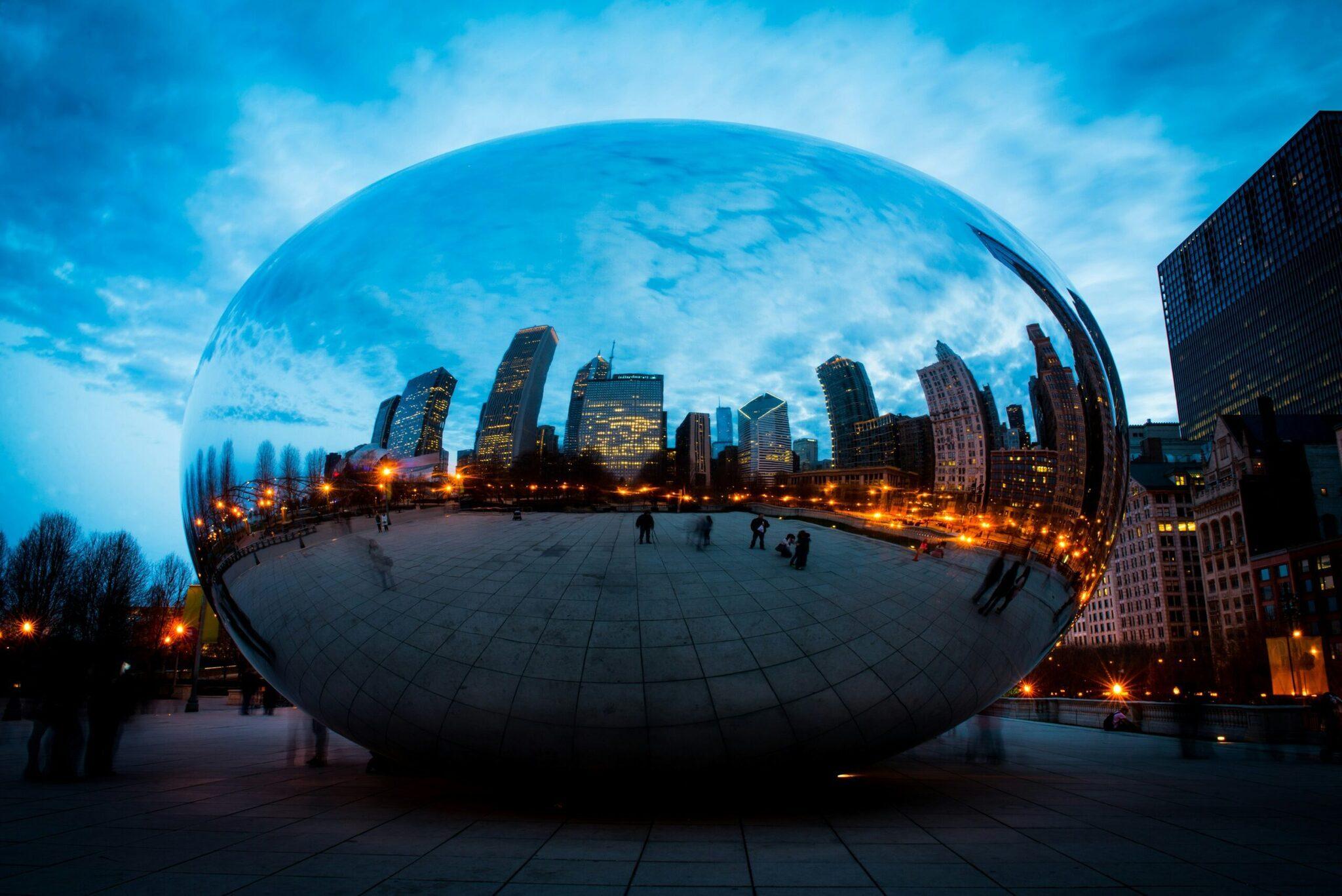 Riesige polierte Stahlskulptur, die die Skyline einer modernen Großstadt in der Abenddämmerung widerspiegelt