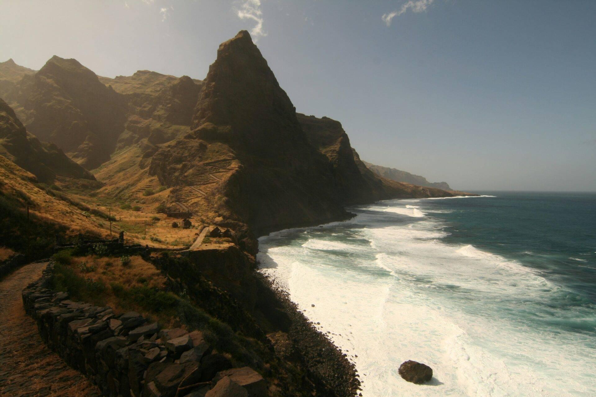 Dramatic rocky cliff overlooking a wild beach with turquoise waves and an arid coastal landscape