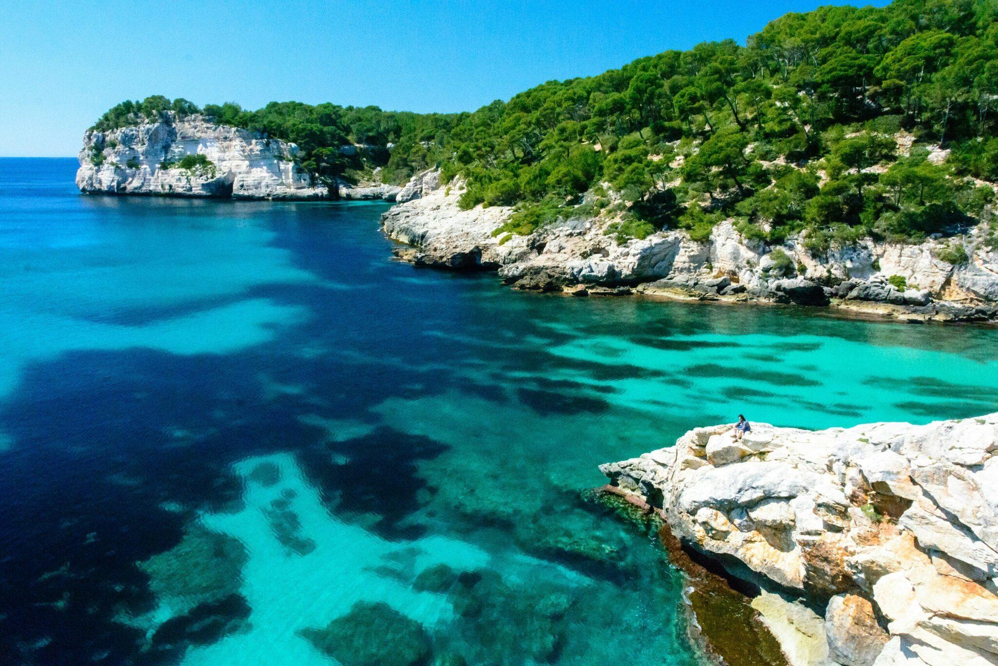 Una cala mediterránea de aguas turquesas cristalinas bordeada de acantilados calizos y vegetación exuberante