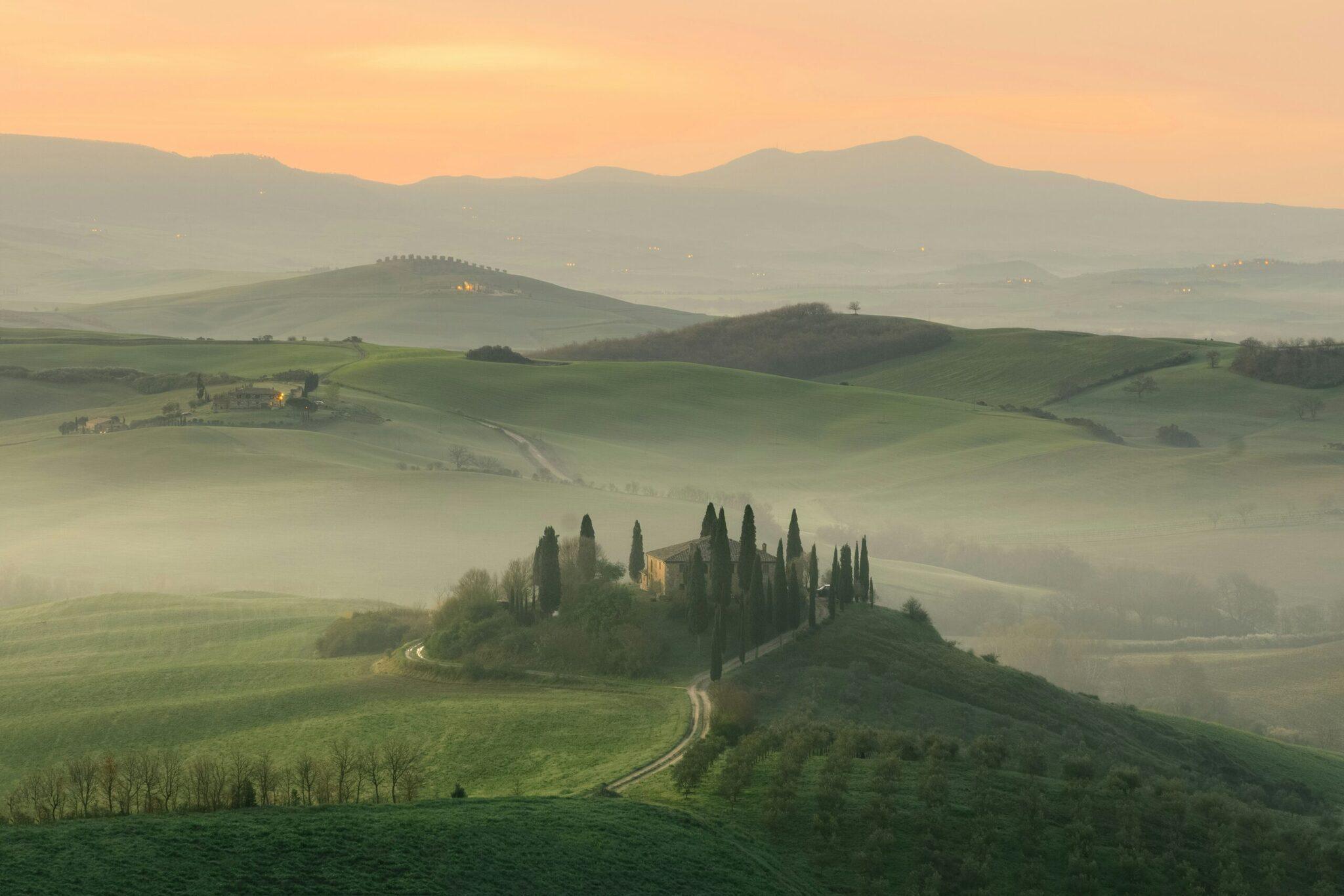 Una villa toscana circondata da cipressi in un paesaggio collinare nebbioso all’alba
