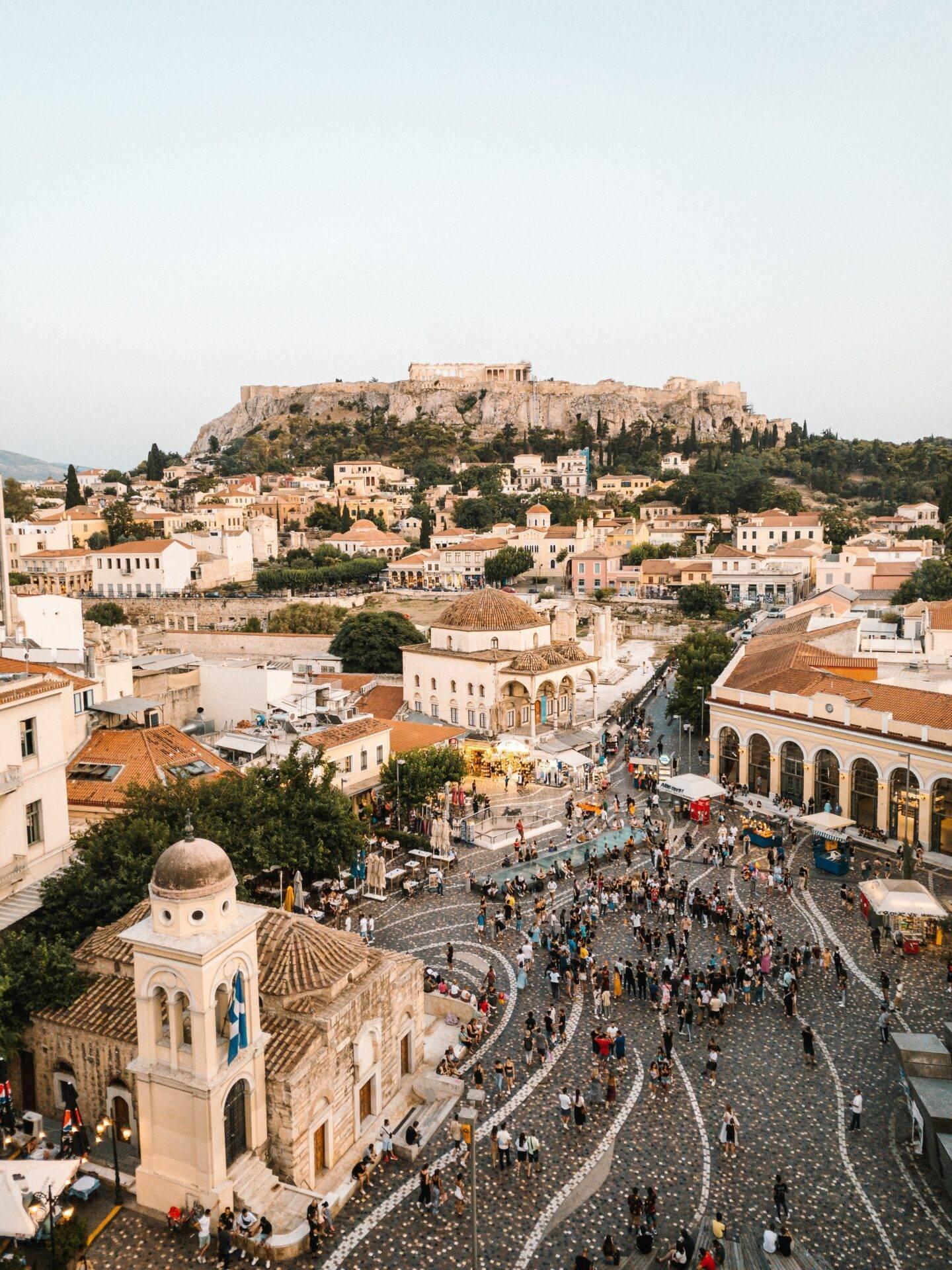 Luftaufnahme eines historischen Platzes mit byzantinischer Kirche, antiker Akropolis im Hintergrund und typischer mediterraner Architektur