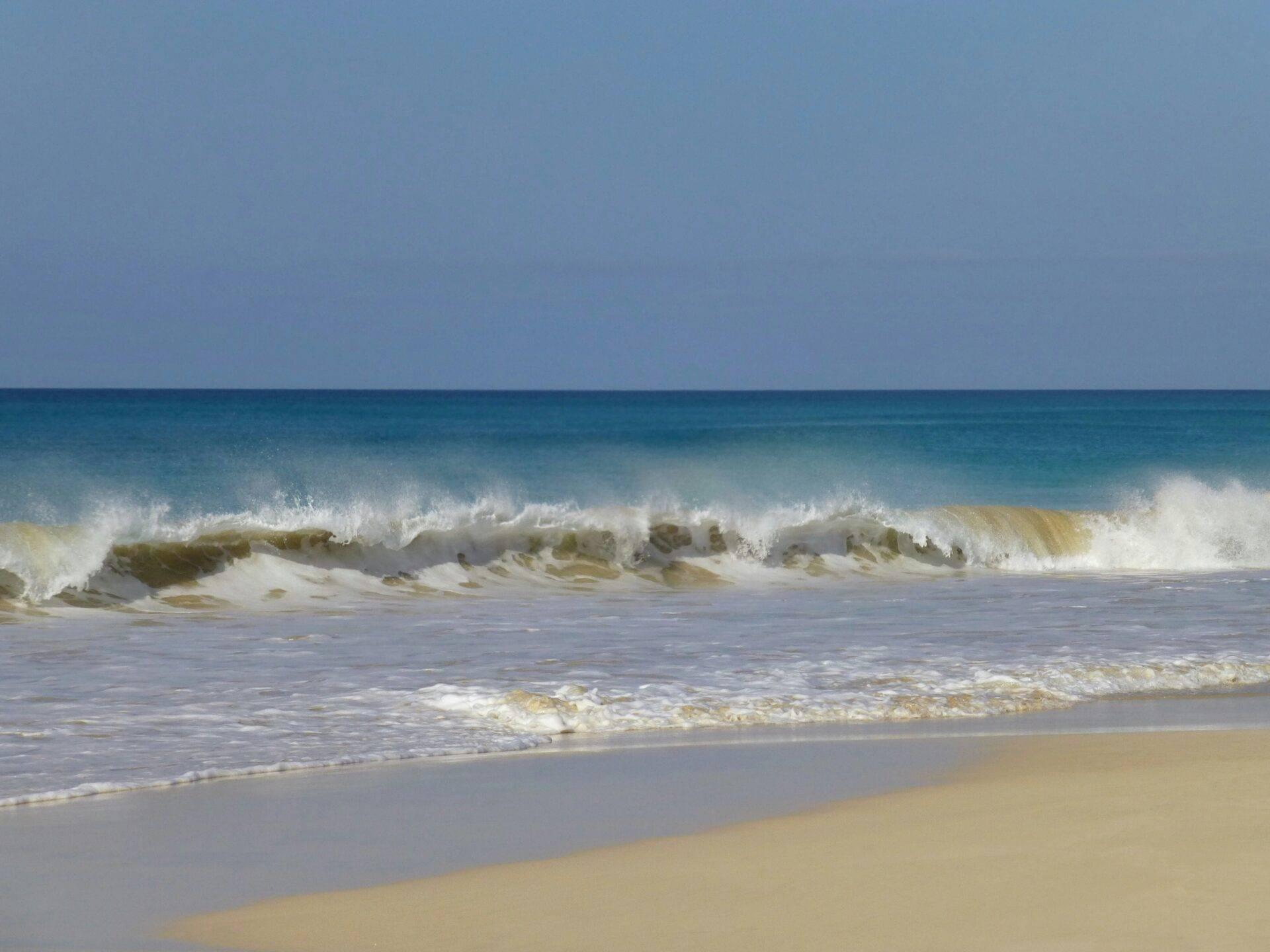 Waves breaking on fine sand under a clear blue sky, peaceful ocean atmosphere
