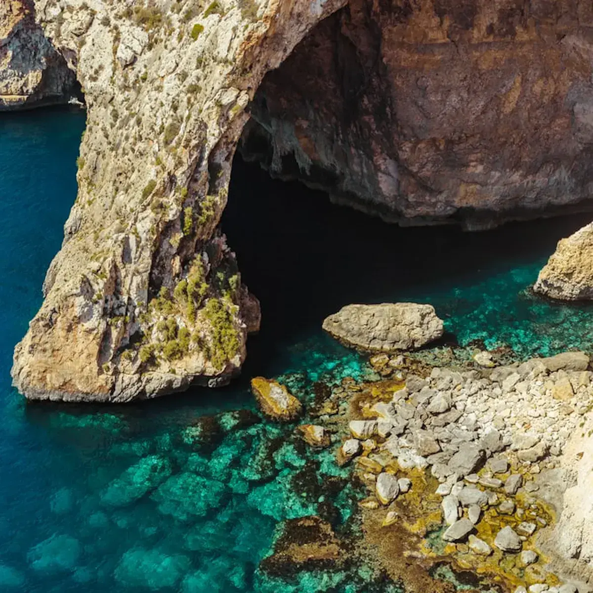 Küstengrotte aus Kalkstein über kristallklarem türkisfarbenem Wasser und farbigen Felsen