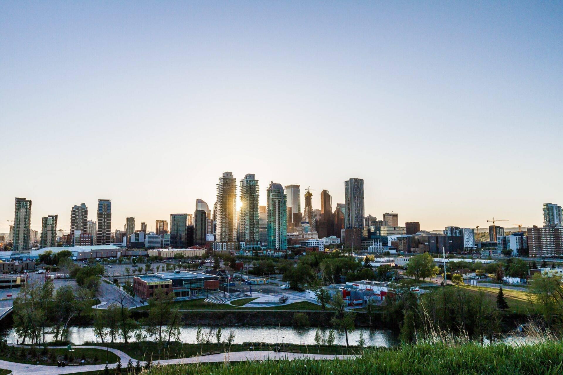 Skyline einer großen kanadischen Stadt bei Sonnenuntergang mit modernen Hochhäusern und einem Fluss im Vordergrund