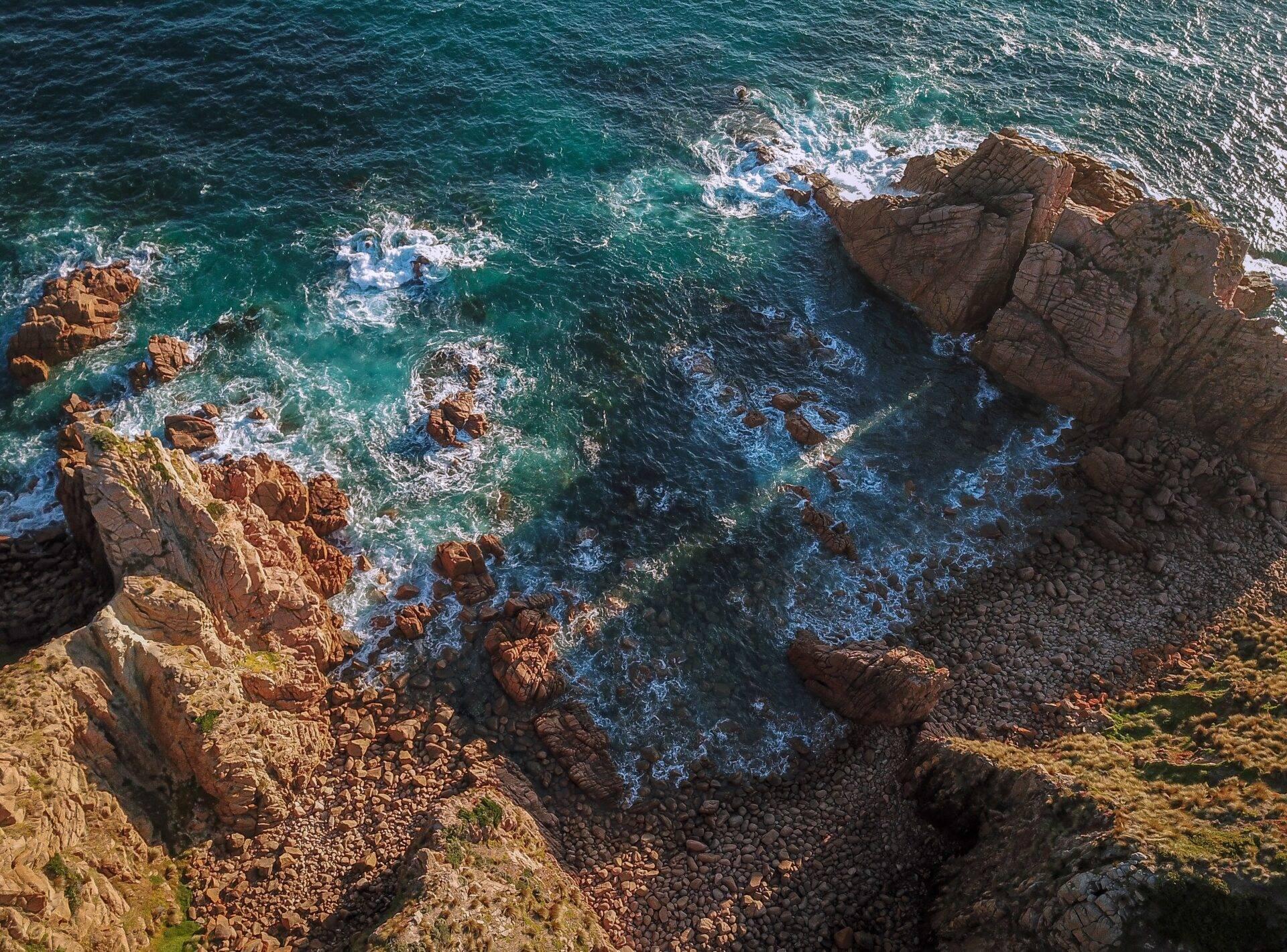 Vista aerea di una costa rocciosa con scogliere rosse, onde turchesi e spettacolari formazioni geologiche