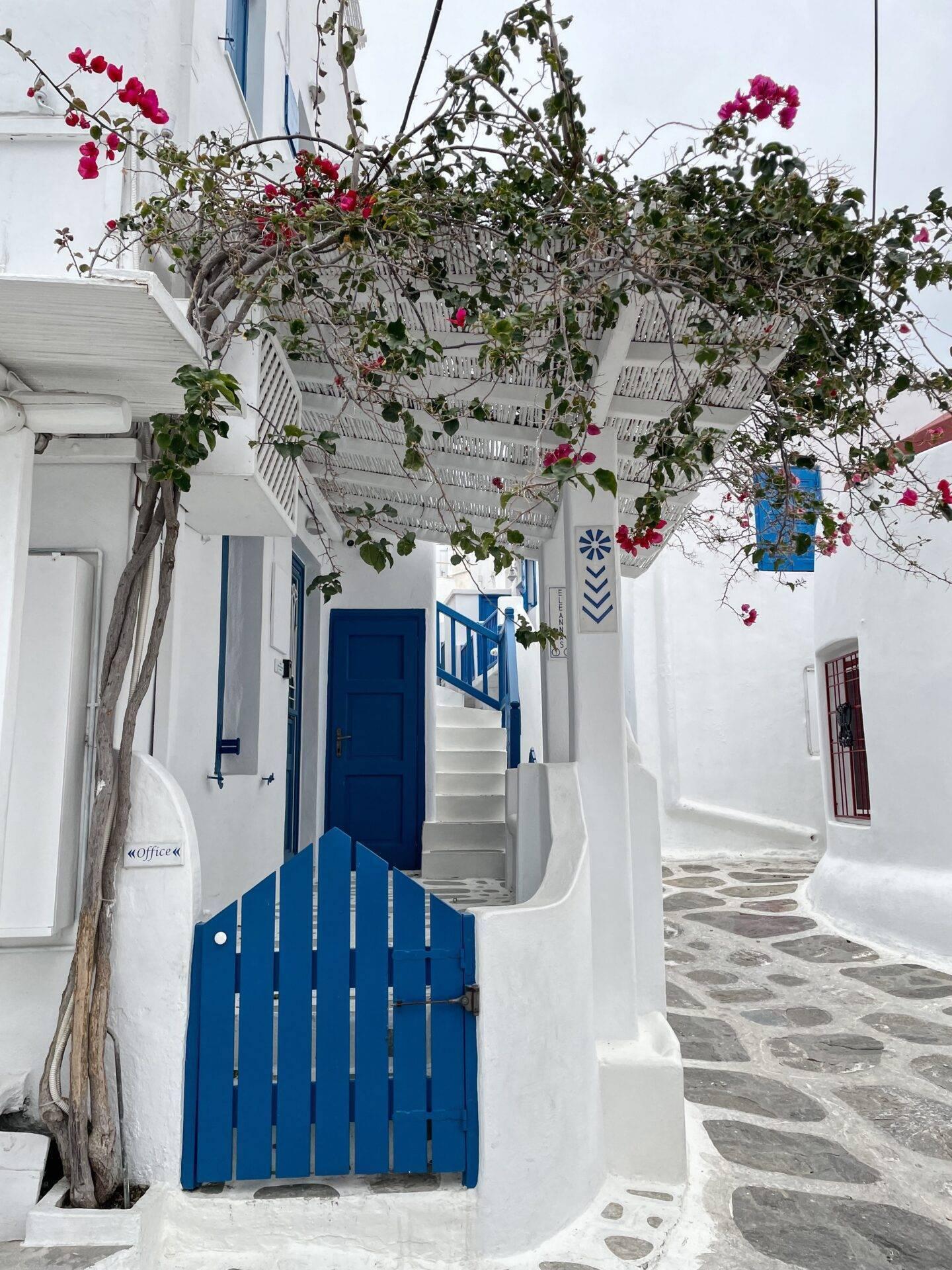 Vicolo mediterraneo con case bianche, porte blu e bouganville rosa in fiore