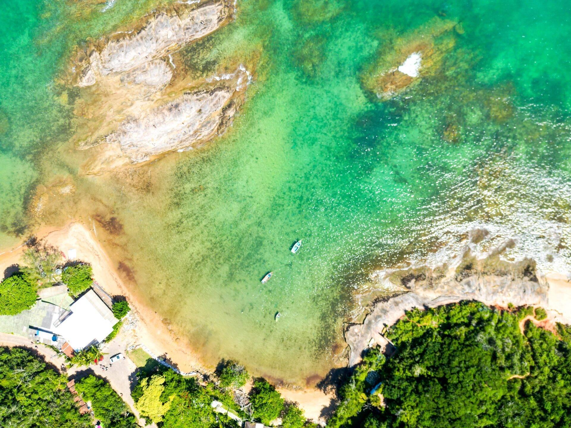 Luftaufnahme einer kleinen Küstenbucht mit Sandstrand, kristallklarem türkisfarbenem Wasser und weißen Felsformationen